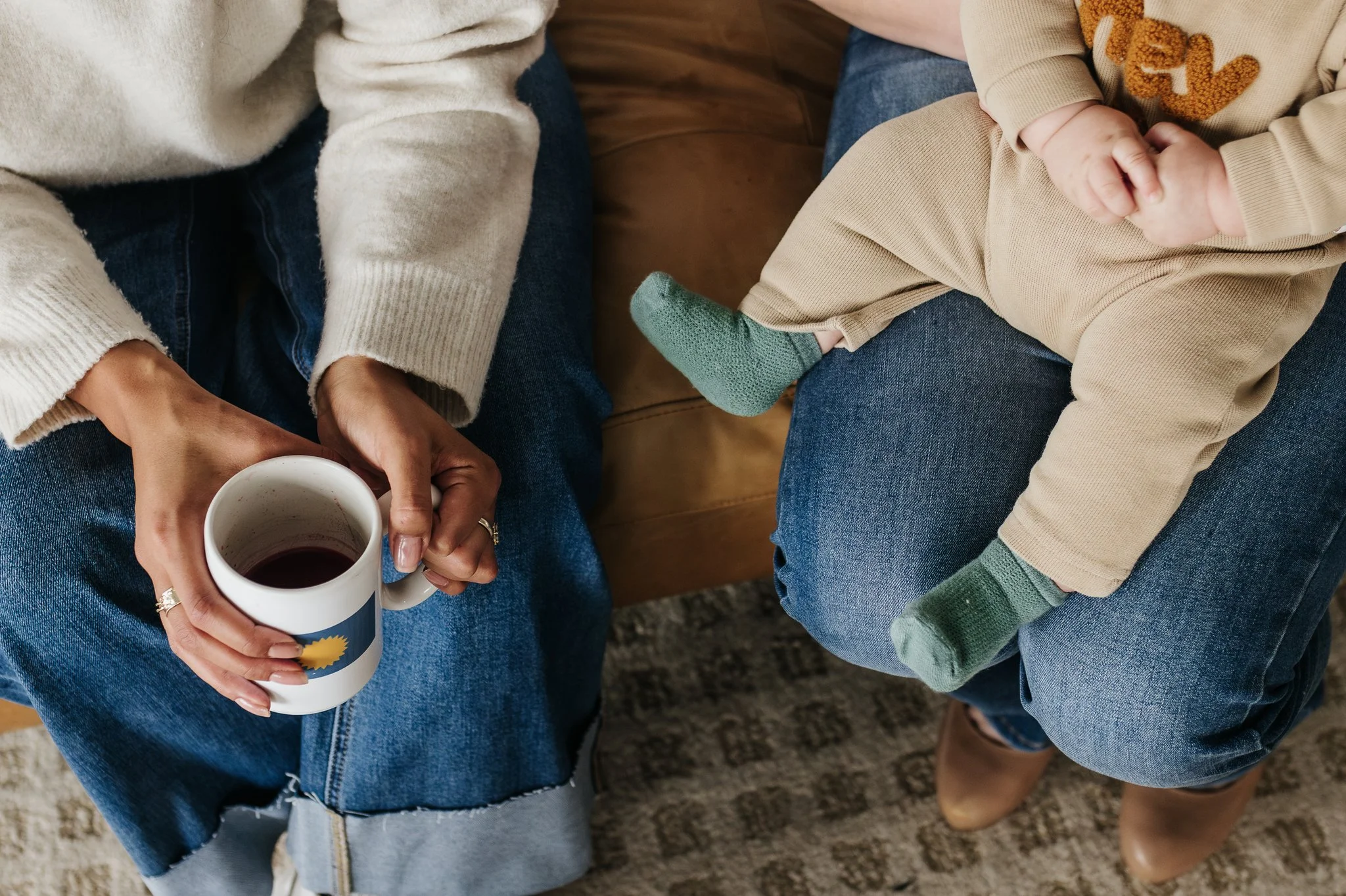 A woman holds a coffee cup and another person holds a young infant.  It's a close up, with no faces.