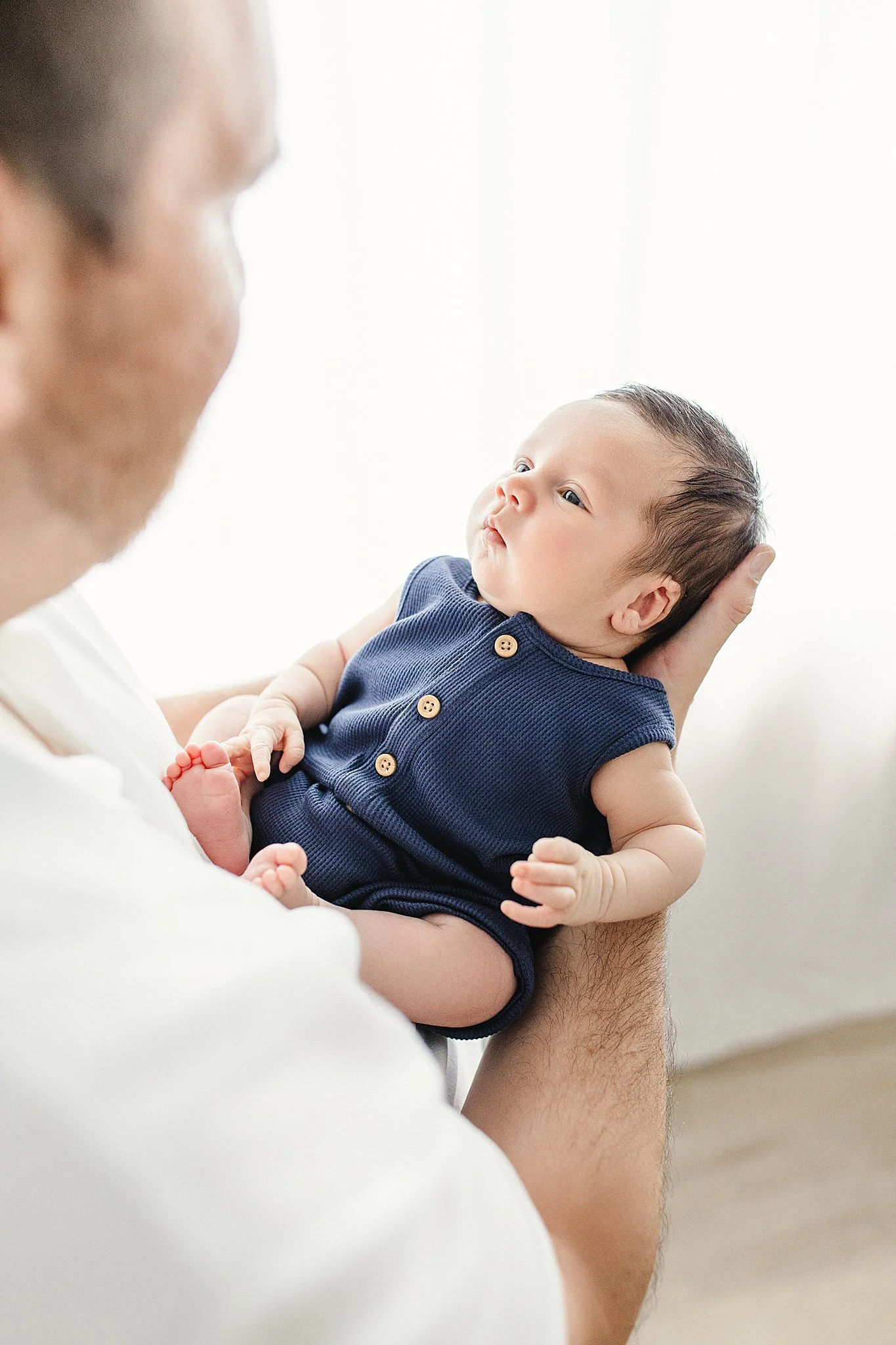 A baby being held by an adult, looking at the adult's face, with only part of the adult's face visible during newborn photos with Ally and B Photography in Naperville, IL.