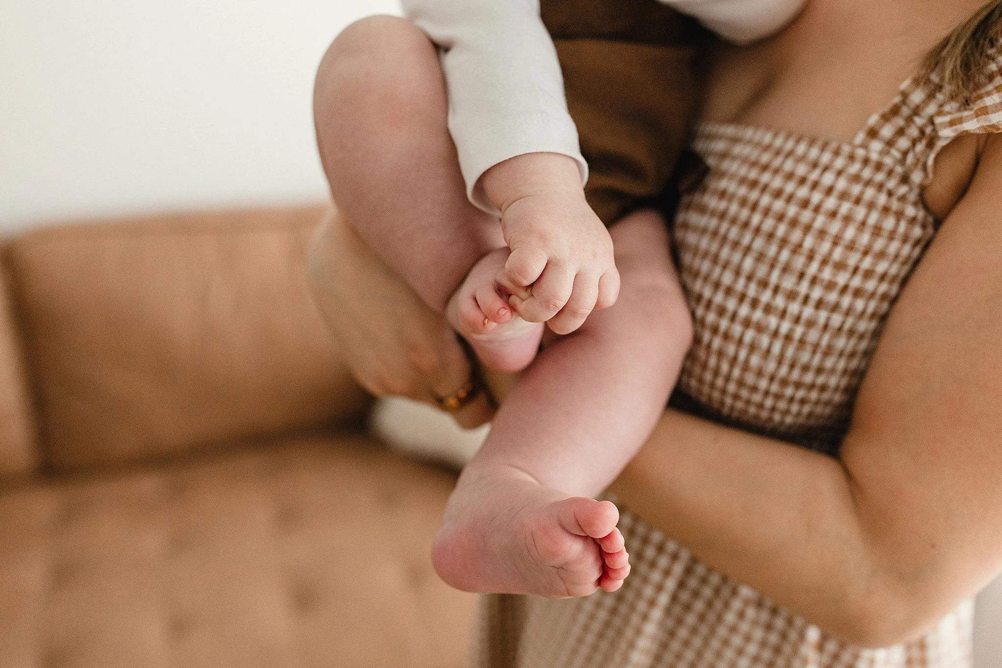 A baby being held by an adult, showing the baby's hand gripping the adult's finger and the baby's foot, with the adult supporting them during lifestyle photos in downtown Naperville, IL.