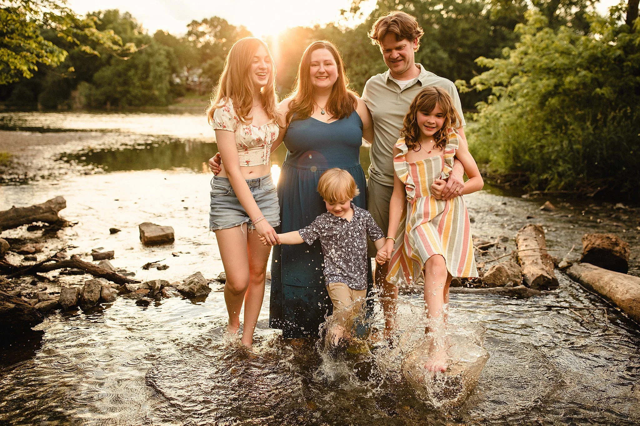 Family of five walking through a shallow creek at sunset during a Naperville family photography session with Ally and B Photography.