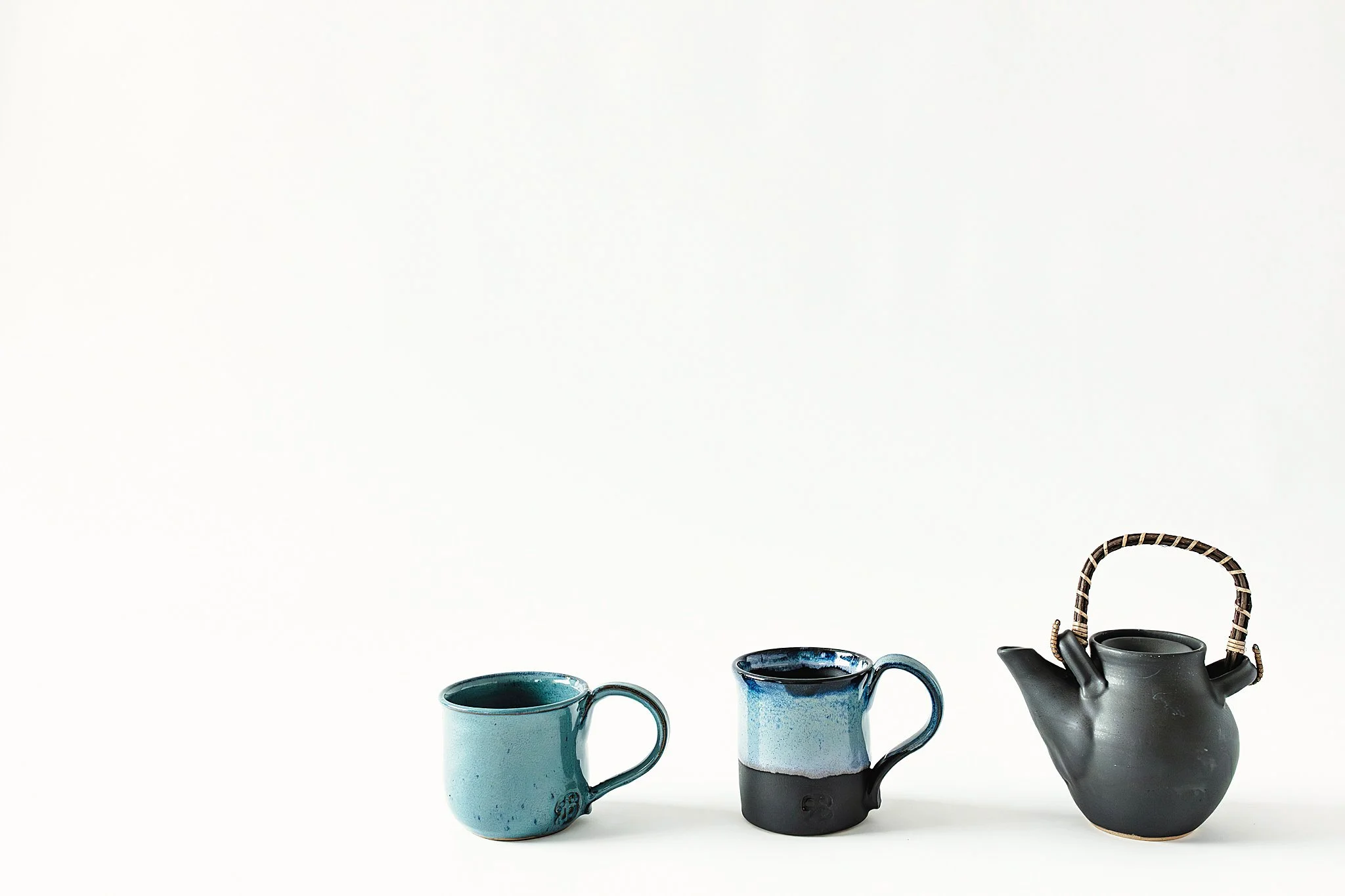 Three ceramic mugs and a teapot arranged in a row on a white background for product photography near me.