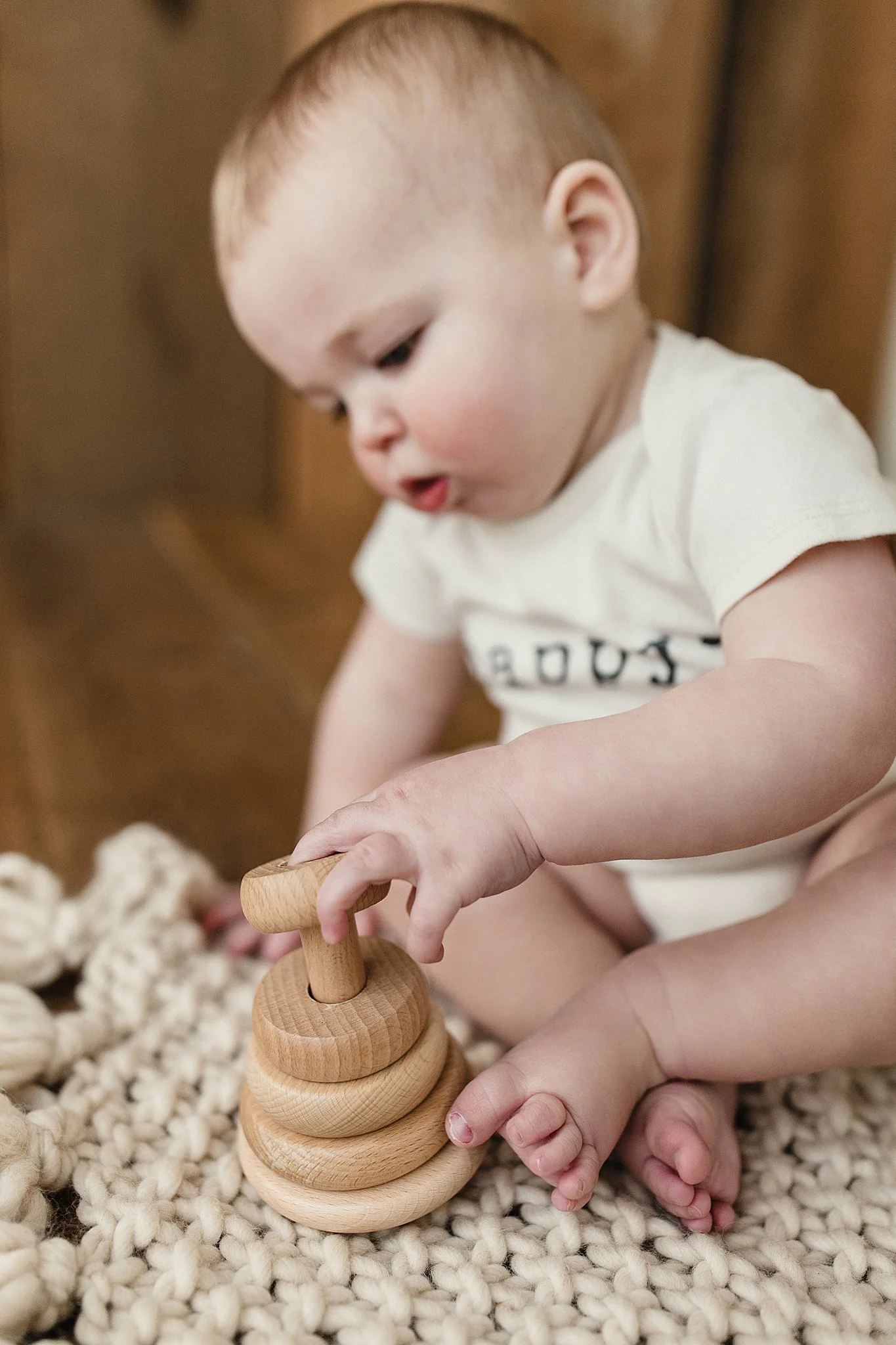 A young child with light skin and red hair playing with a wooden spinning top toy on a textured blanket with the best Naperville baby photographer.