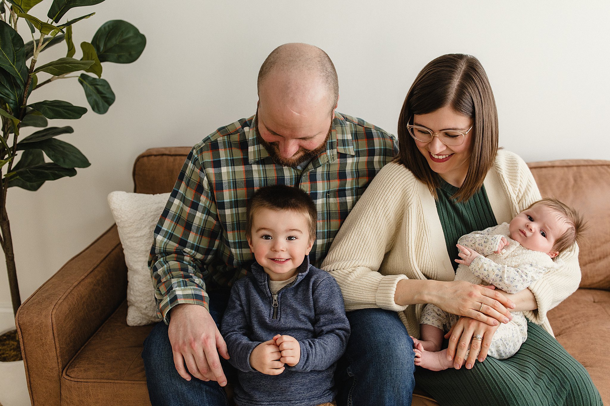 A family of five sitting on a brown sofa, including two children and two adults, smiling and enjoying time together at home with family photographers in Naperville.