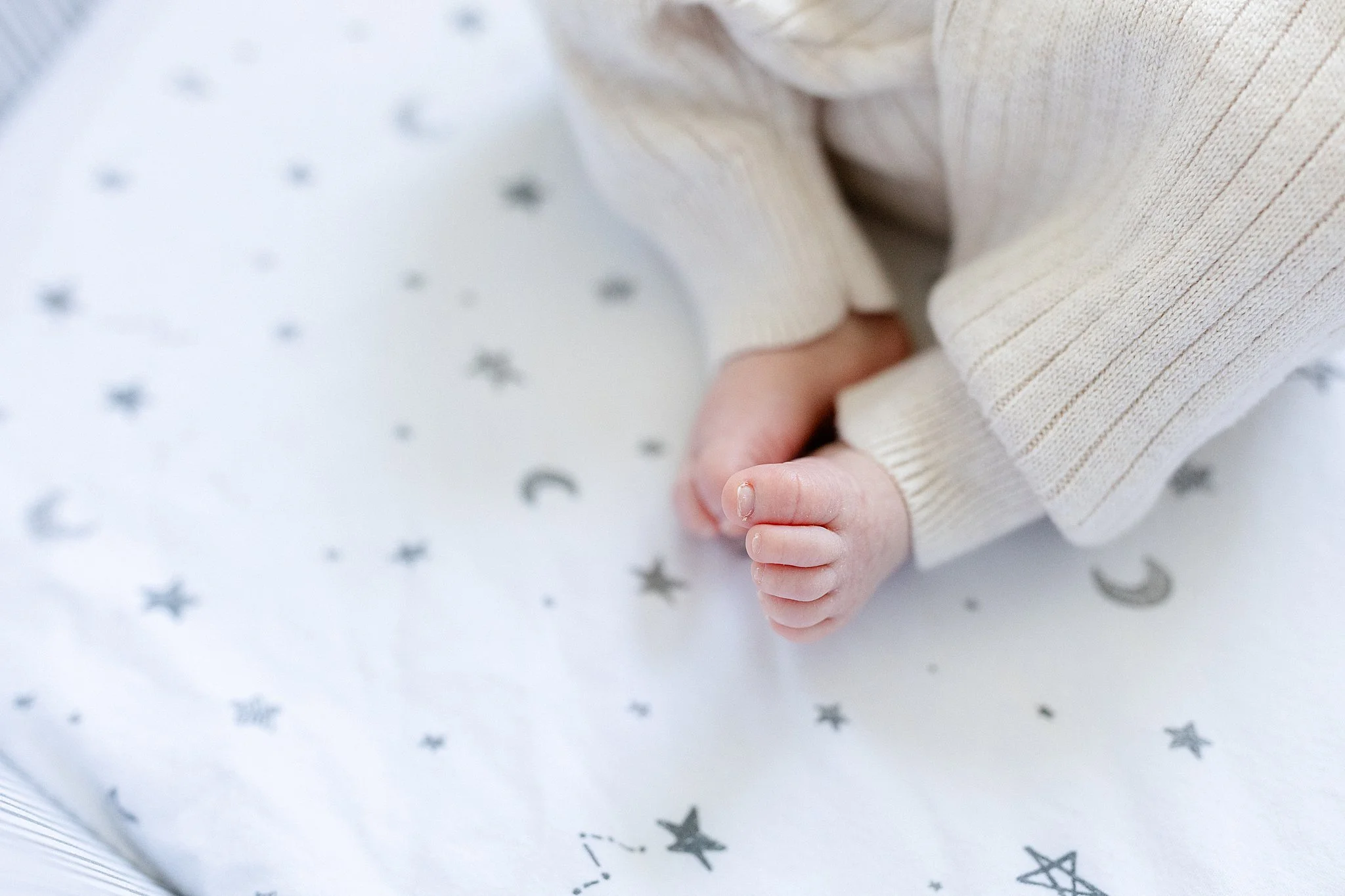 Close-up of a baby's hand holding onto a fabric with star patterns, with the baby wearing a cream-colored knit sweater in home newborn photography Elmhurst.