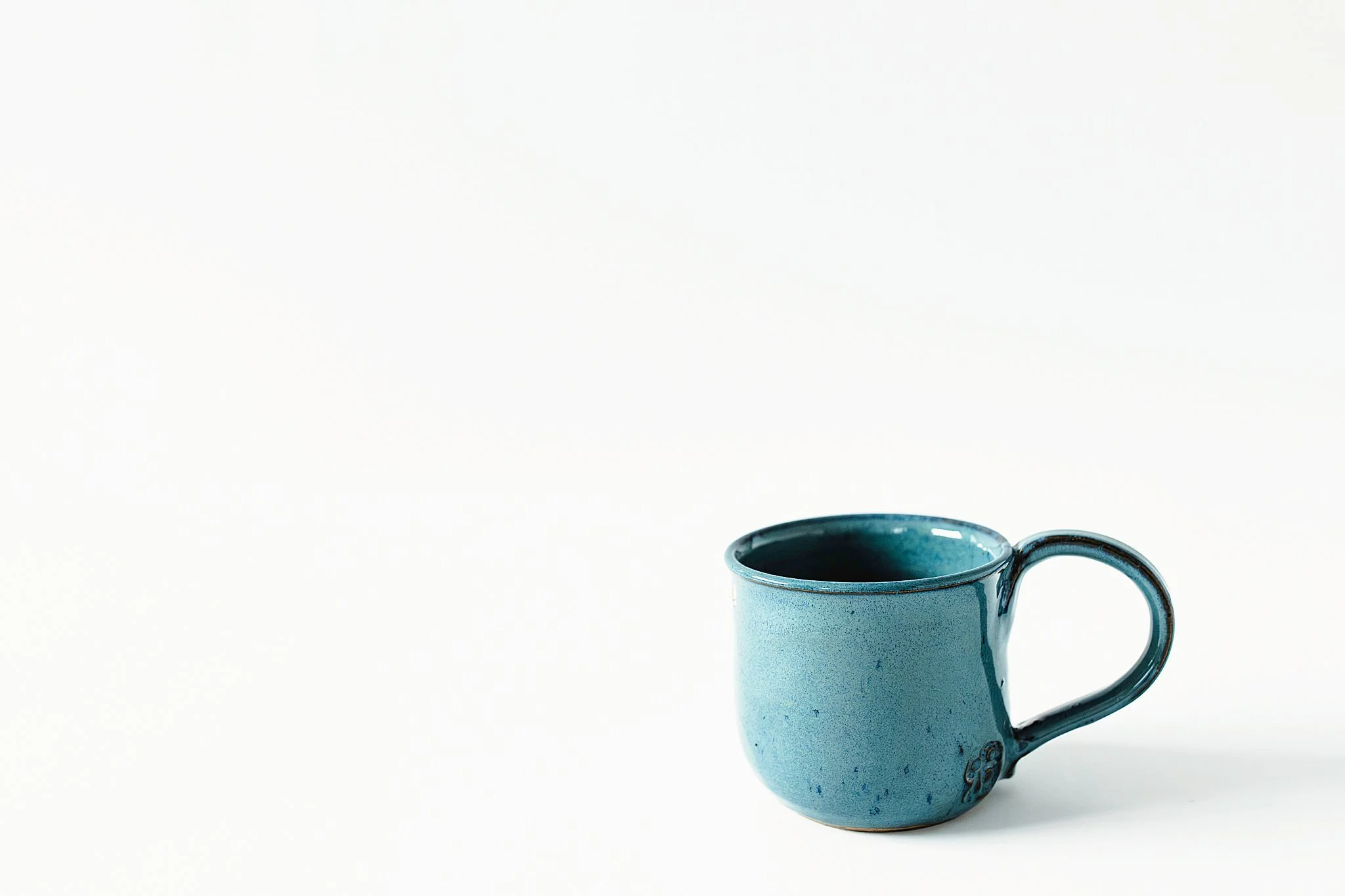 A blue ceramic mug filled with a dark liquid, placed on a white background for Naperville product photography.