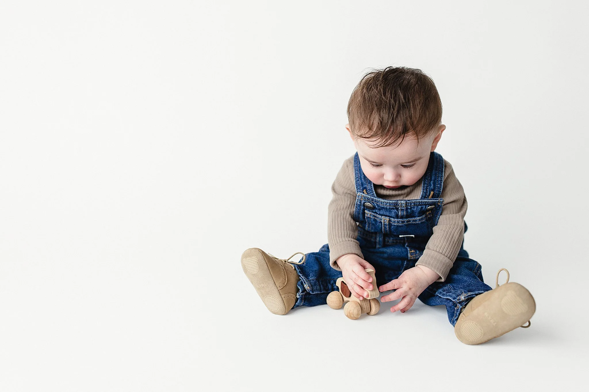 Cute baby sitting on white background, playing with wooden toy animal