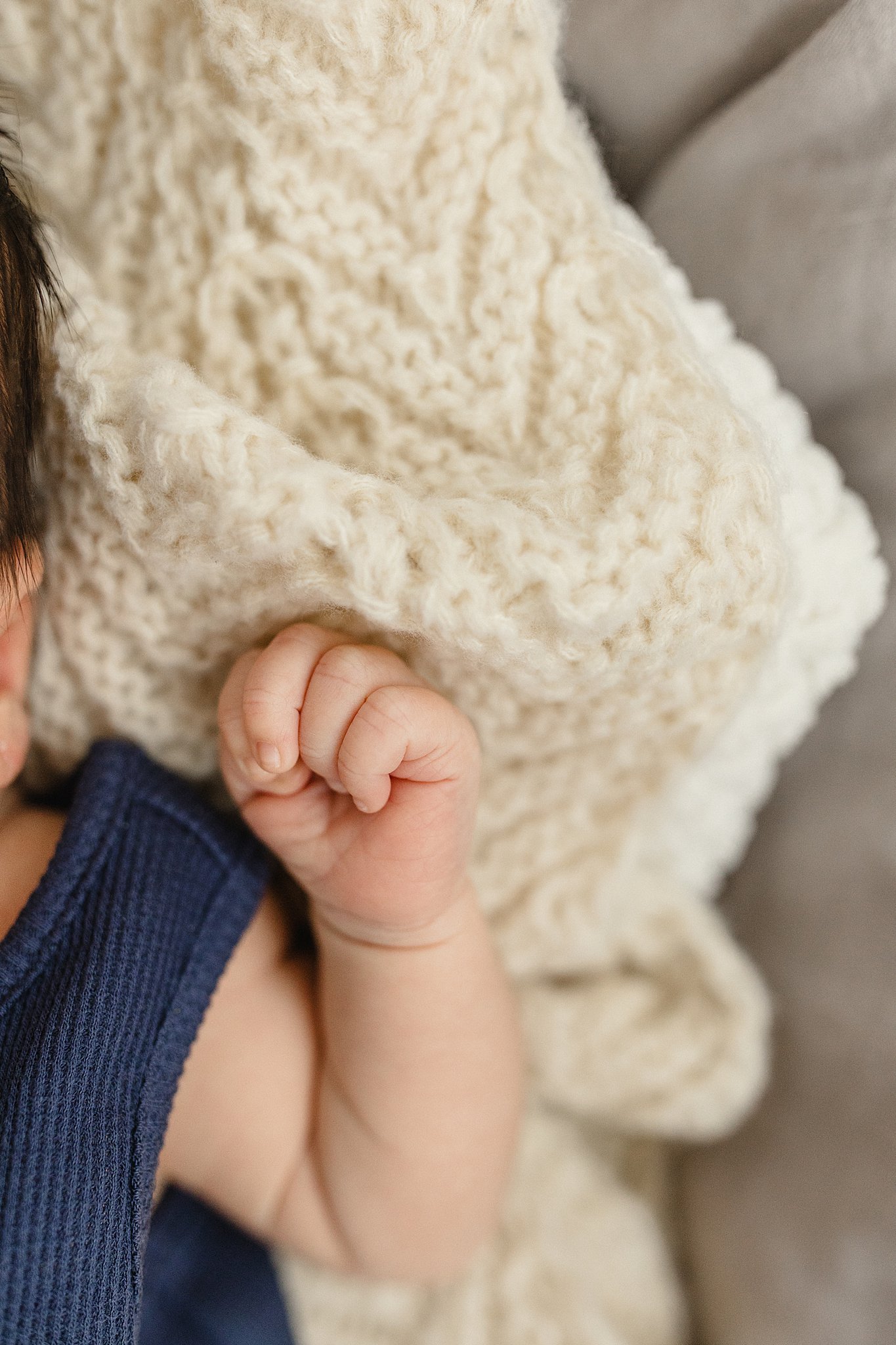 Close-up of a child's hand holding an adult's hand, with a cozy cream-colored sweater in the background for newborn photography  near me.