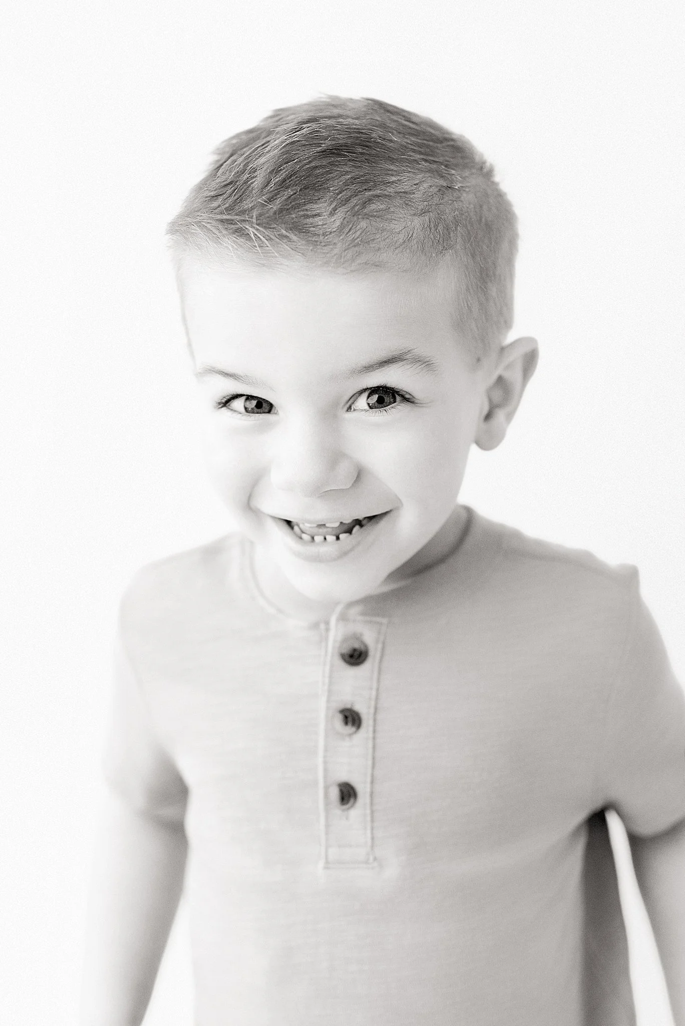Black and white photo of a smiling young boy with short hair, wearing a shirt with four buttons during a personality mini in Naperville, IL.