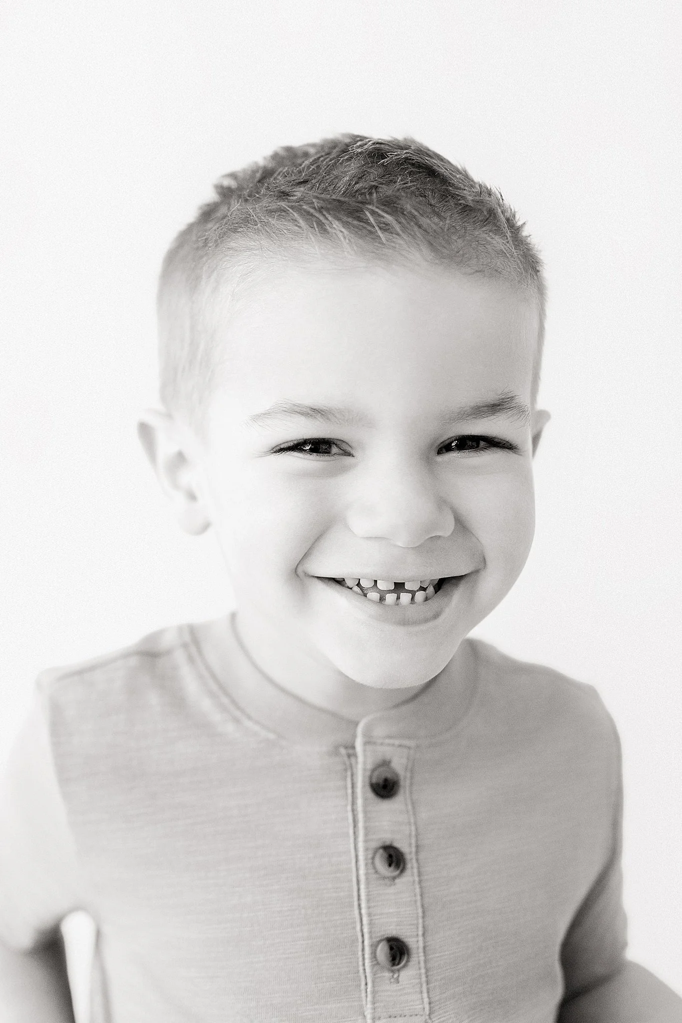 A smiling young boy with short hair, wearing a light-colored shirt with buttons, in black and white during a downtown Naperville photoshoot.