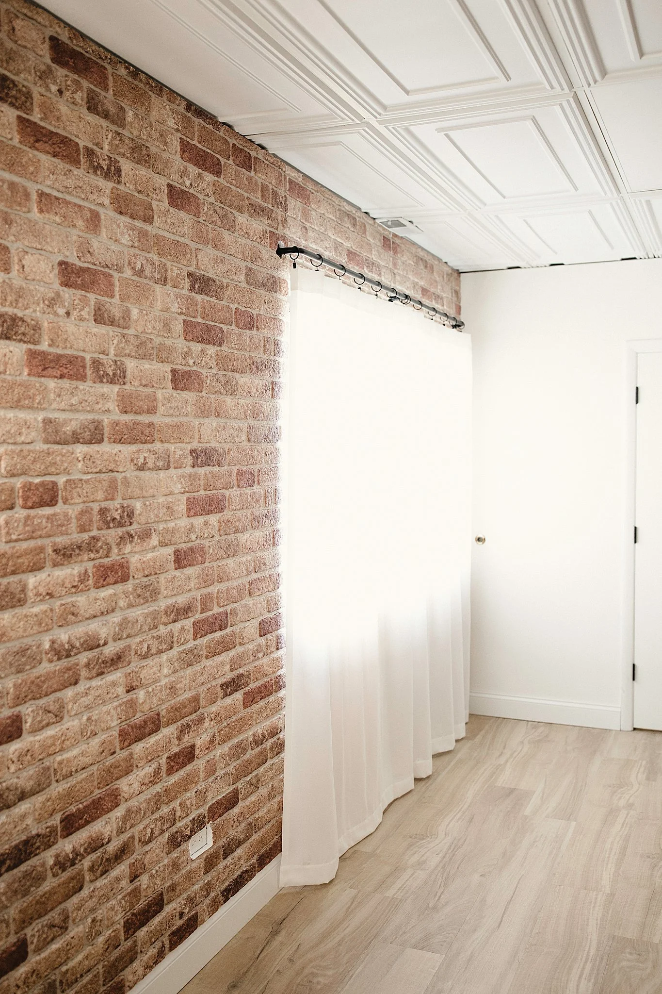 Room with brick accent wall, white curtains, and white door for Naperville photography studios.