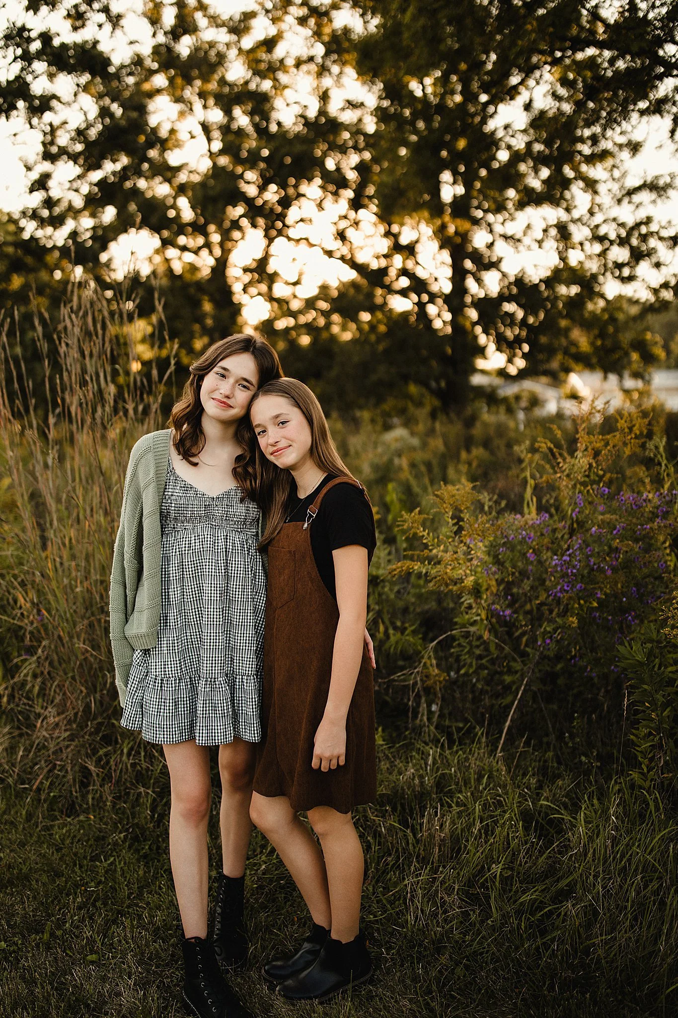 Two young girls standing outdoors in a field during sunset, smiling and embracing each other during a family photoshoot near Naperville, IL.