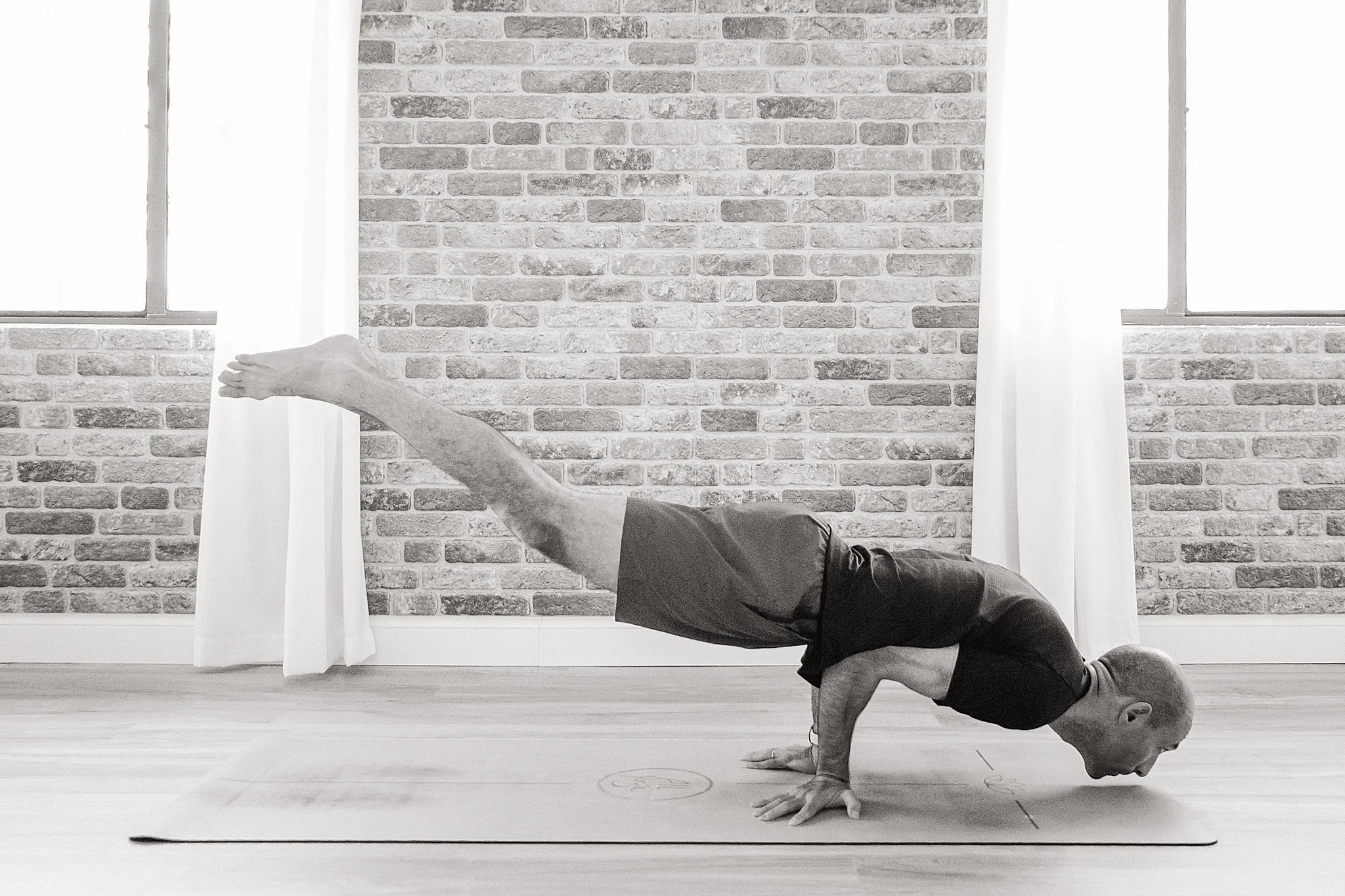 An older man practicing yoga in a room with brick walls and windows, performing a handstand with one leg extended forward during a Naperville personal branding photo session for a yoga instructor.
