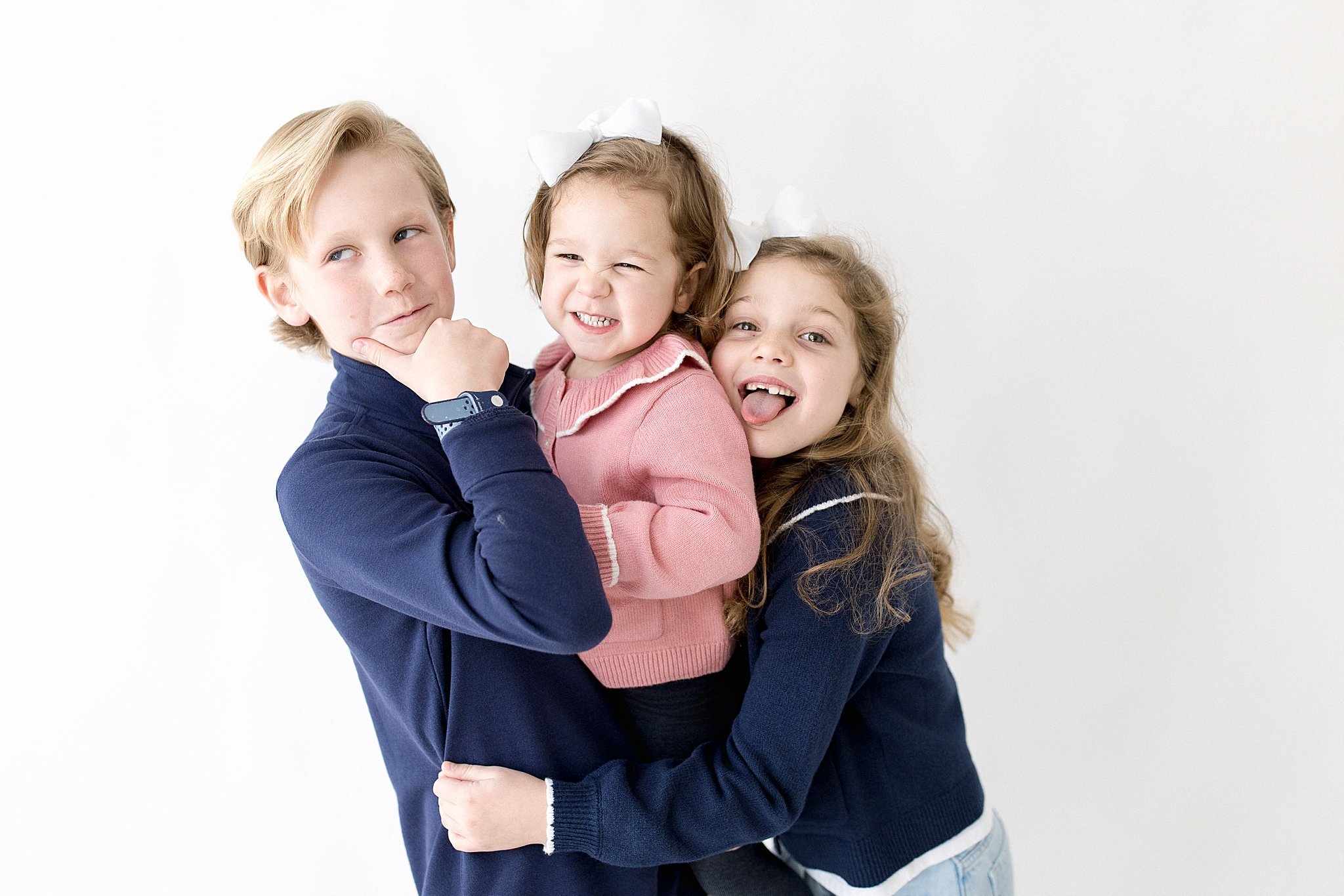Three children, two girls and a boy, posing together against a plain white background during a kids portrait session near me.