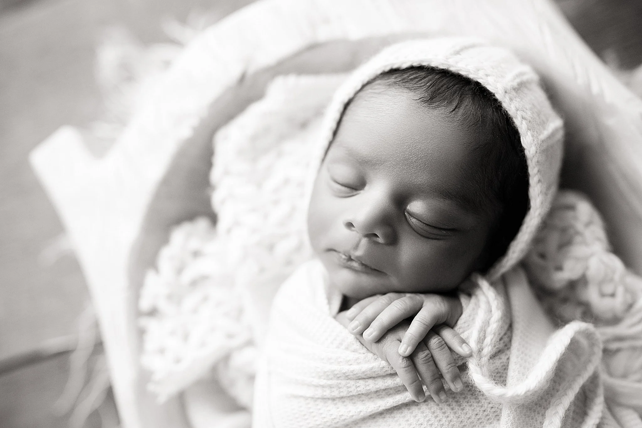 A sleeping baby with a hooded blanket, lying on a soft blanket. Black and white photo for newborn photos near me.