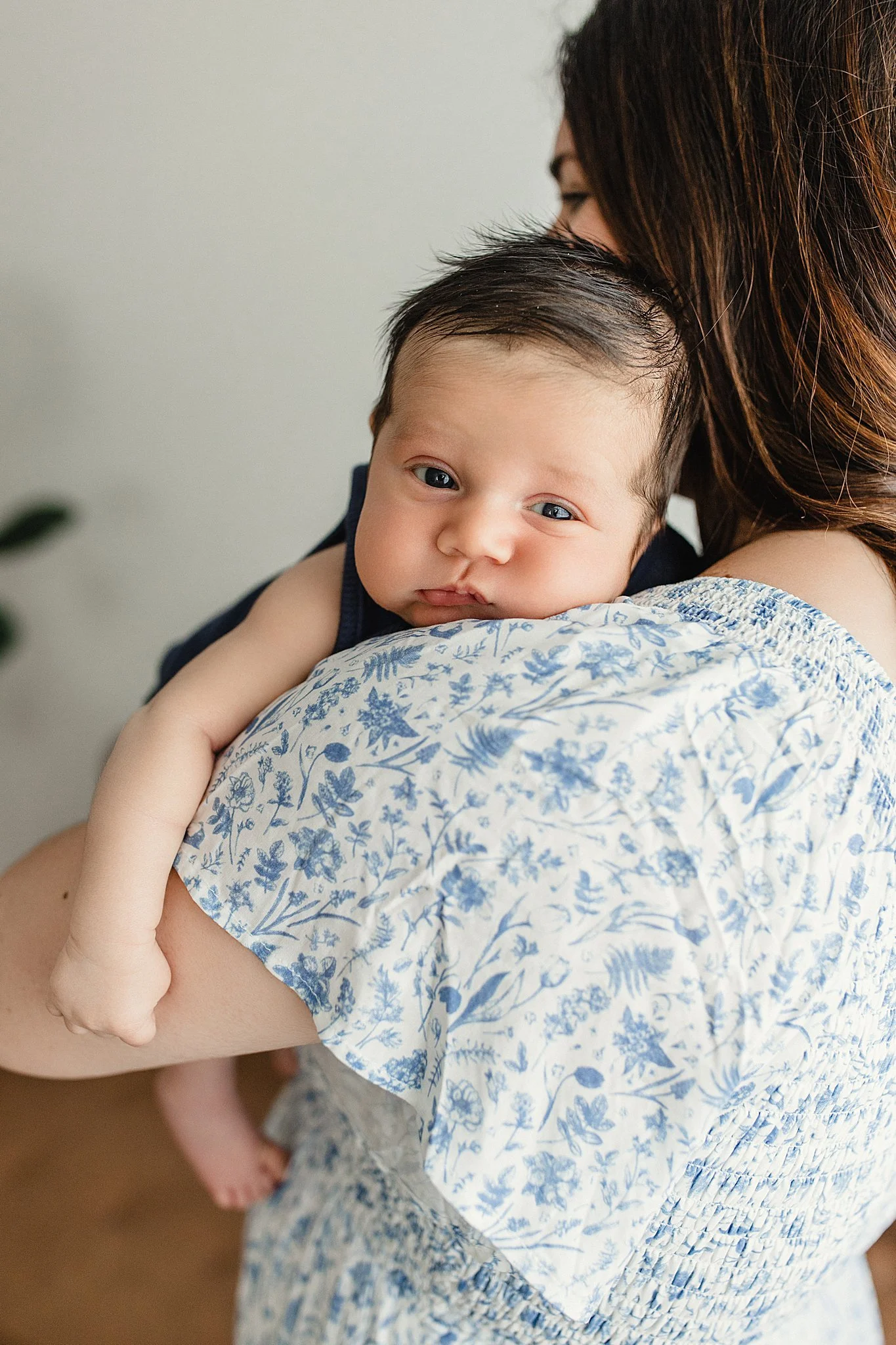 A young child being held by an adult, resting their head on the adult's shoulder, with focused eyes and a calm expression. The child is wearing a sleeveless navy shirt and has short, dark hair during lifestyle newborn photos Naperville.