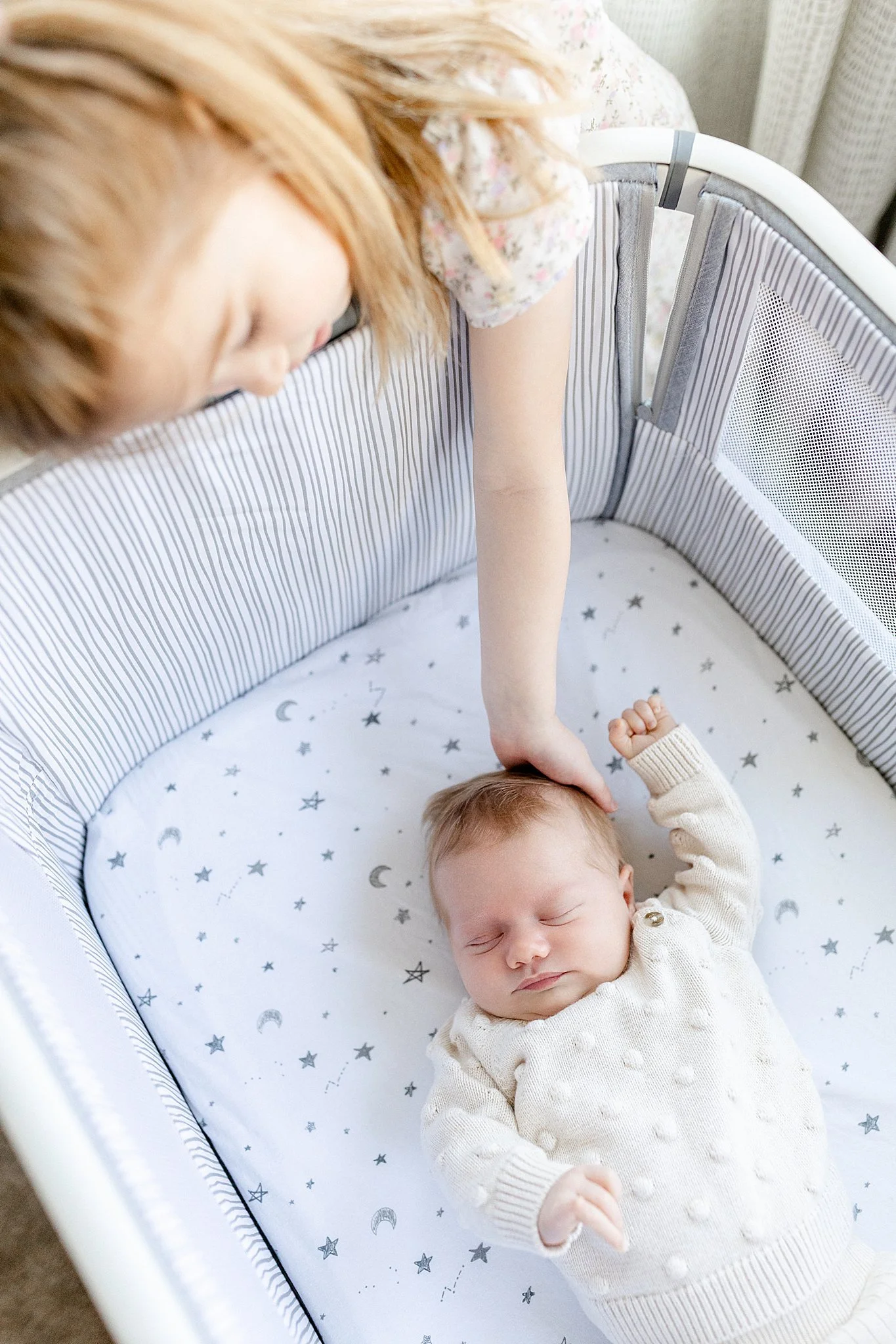 A young child with light hair and wearing a cream-colored sweater is sleeping in a crib with a celestial-themed sheet featuring stars, moons, and clouds with a lifestyle photographer Elmhurst.