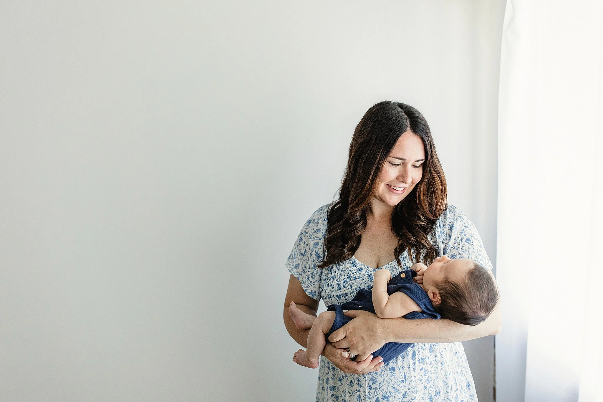 A woman with dark, wavy hair smiling and holding a baby in her arms for lifestyle newborn photography Naperville.