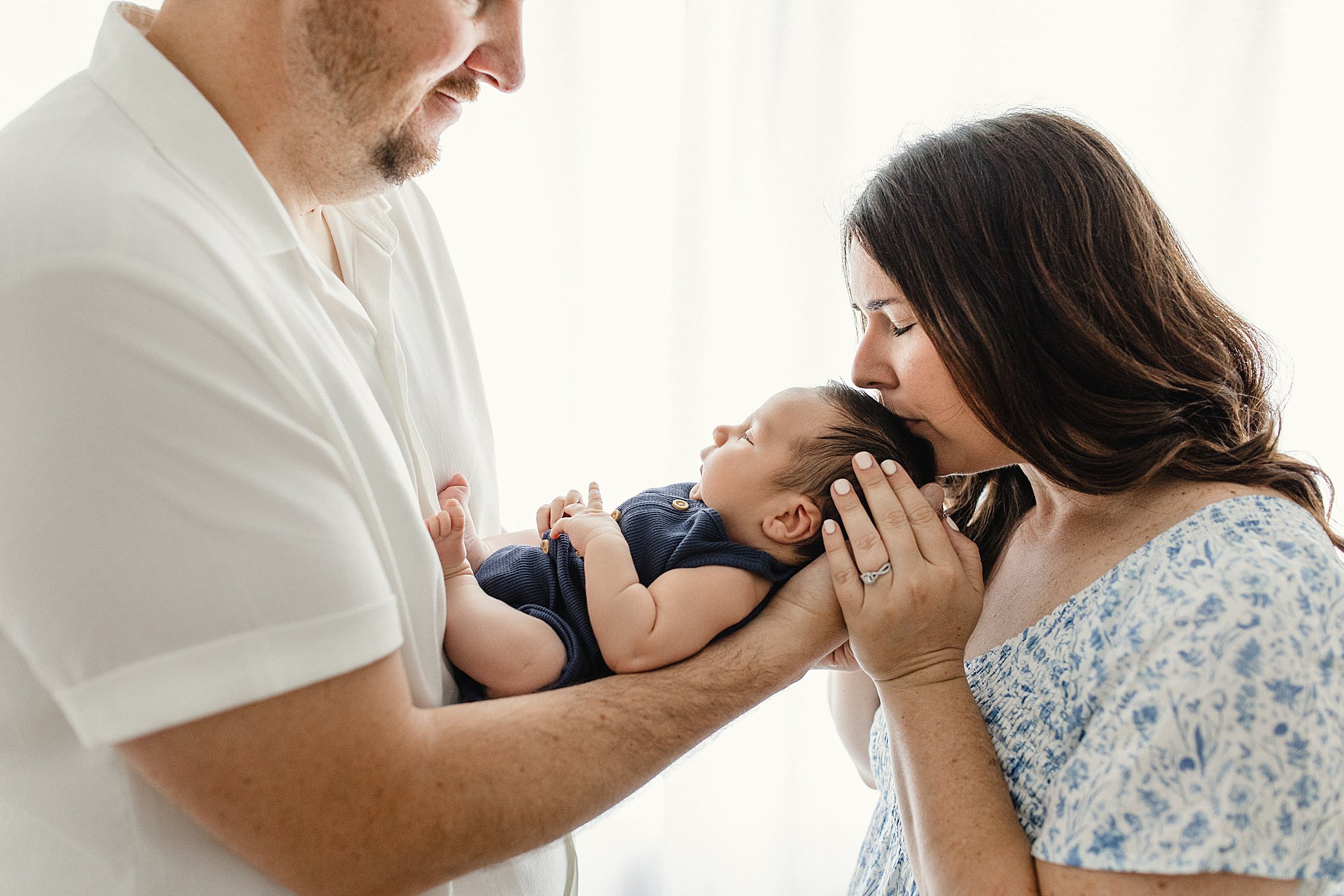 A family with a mother and father holding their baby close in a bright room with a newborn photographer in Naperville.