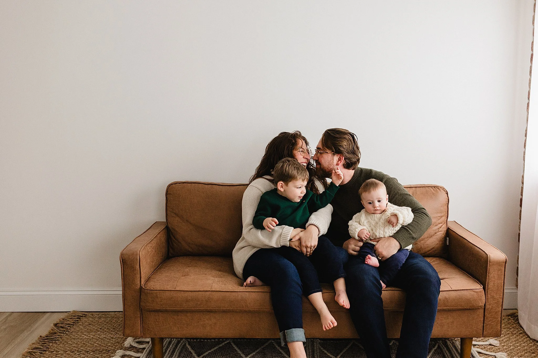 A family of four sitting on a brown couch, hugging and laughing, in a cozy living room during a Naperville family photo session.