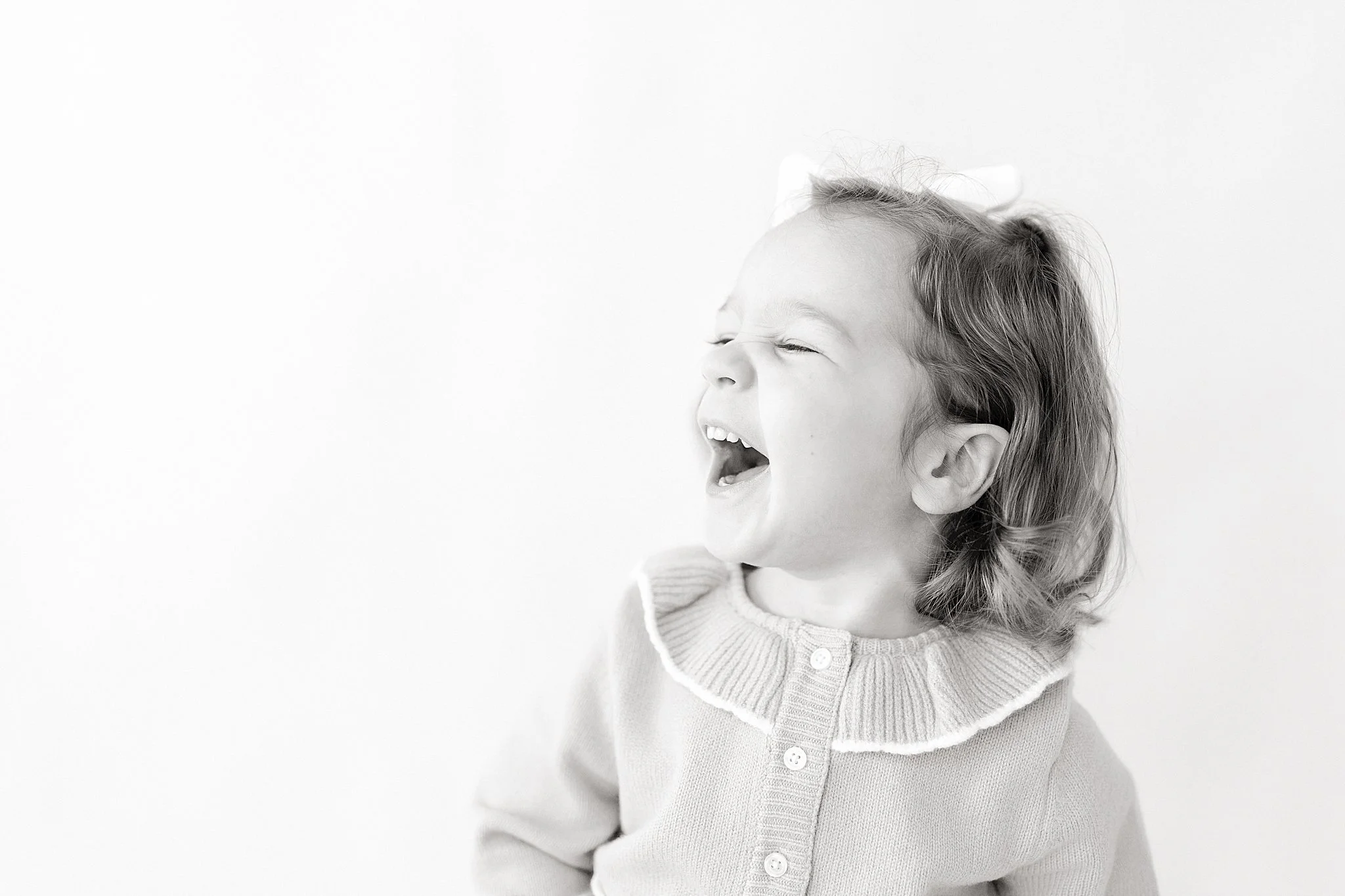 A young girl with curly hair wearing a sweater with a ruffled collar laughing with her eyes closed during a personality minis near me.