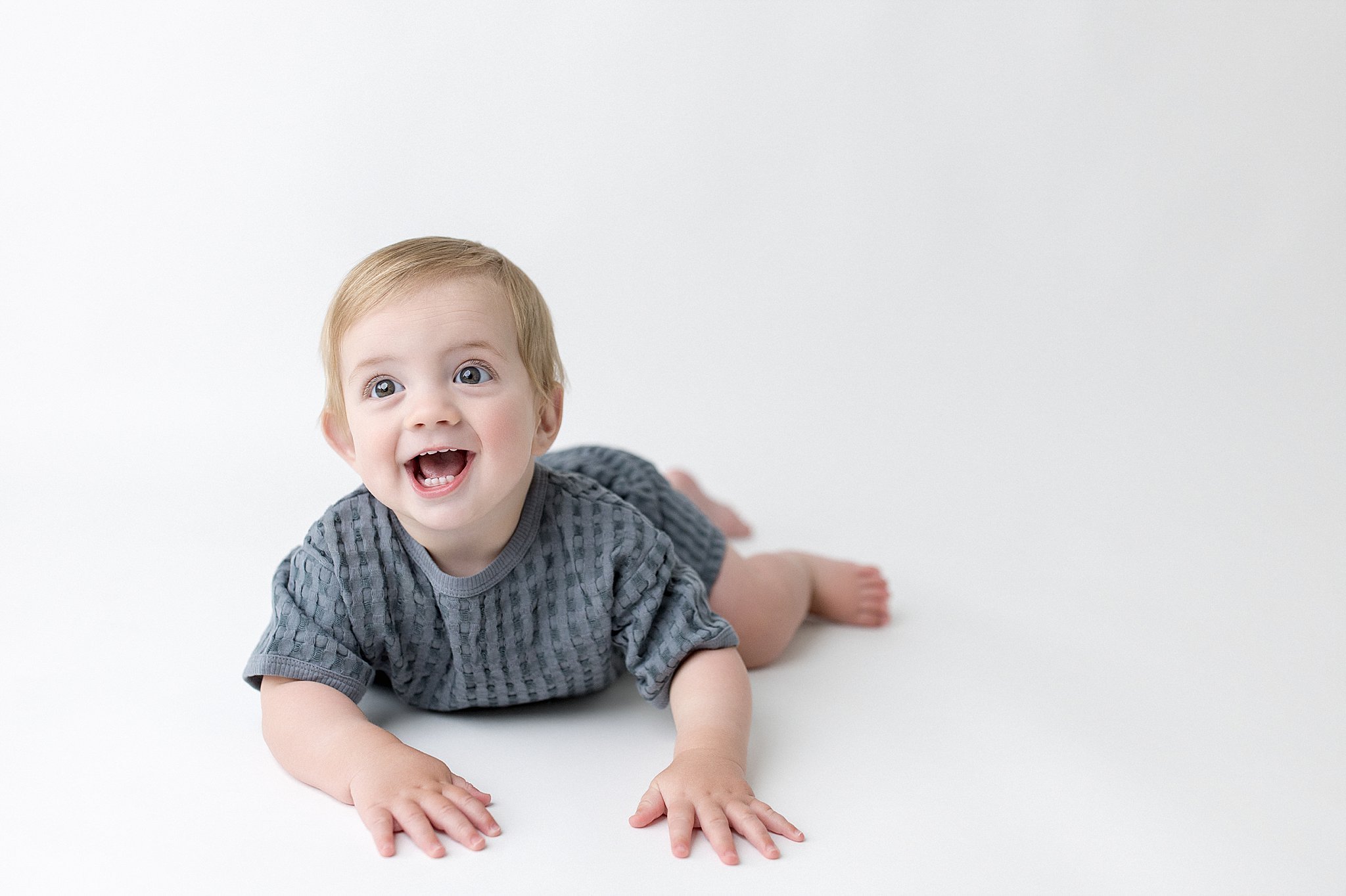 Smiling baby crawling on a white surface during a baby photoshoot in downtown Naperville, IL.