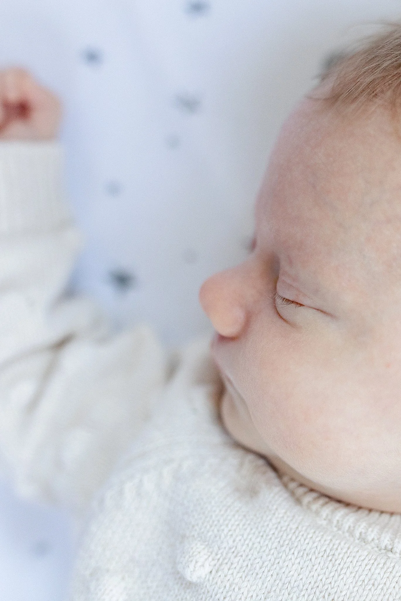Close-up of an infant sleeping peacefully, with only the facial features and part of the head visible, lying on a soft white blanket with a lifestyle photographer Darien, IL.