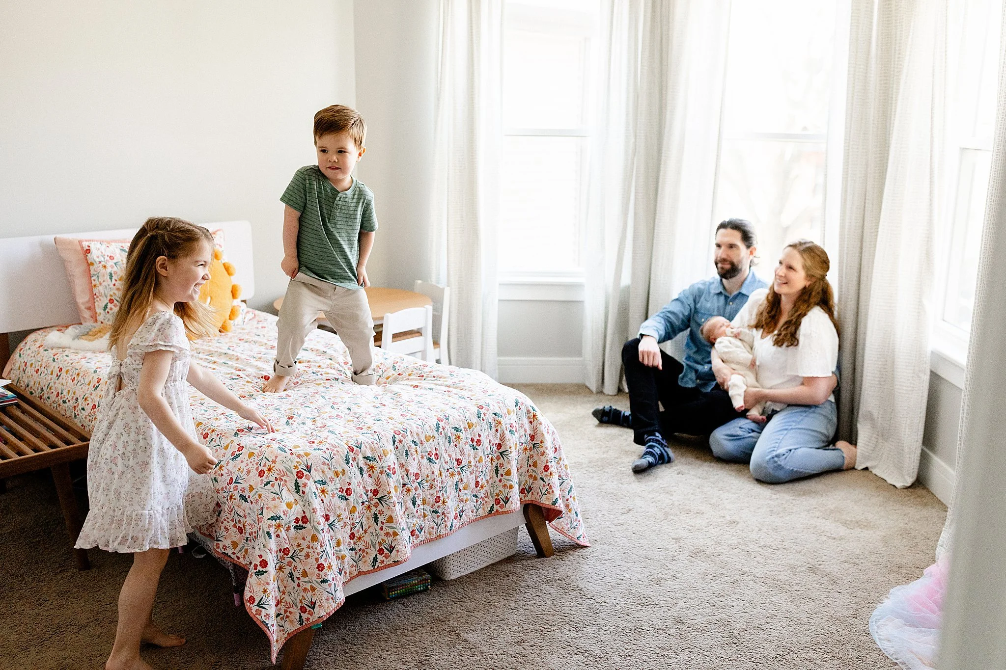 A family of five, including two young girls, a young boy, a man, and a woman, enjoying a moment in a bedroom with natural light with a lifestyle photographer Hinsdale.