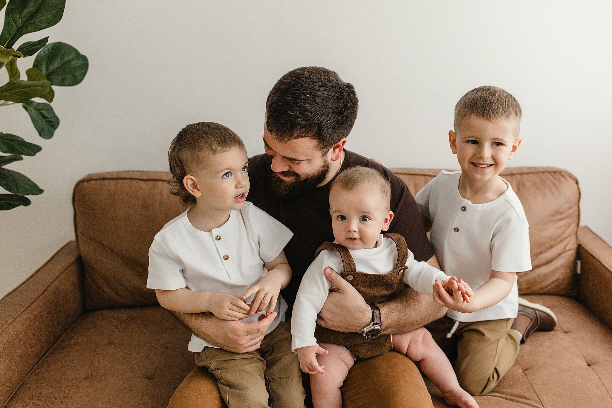 A man with three young children sitting on a brown sofa in a living room for lifestyle photography in Naperville, IL.