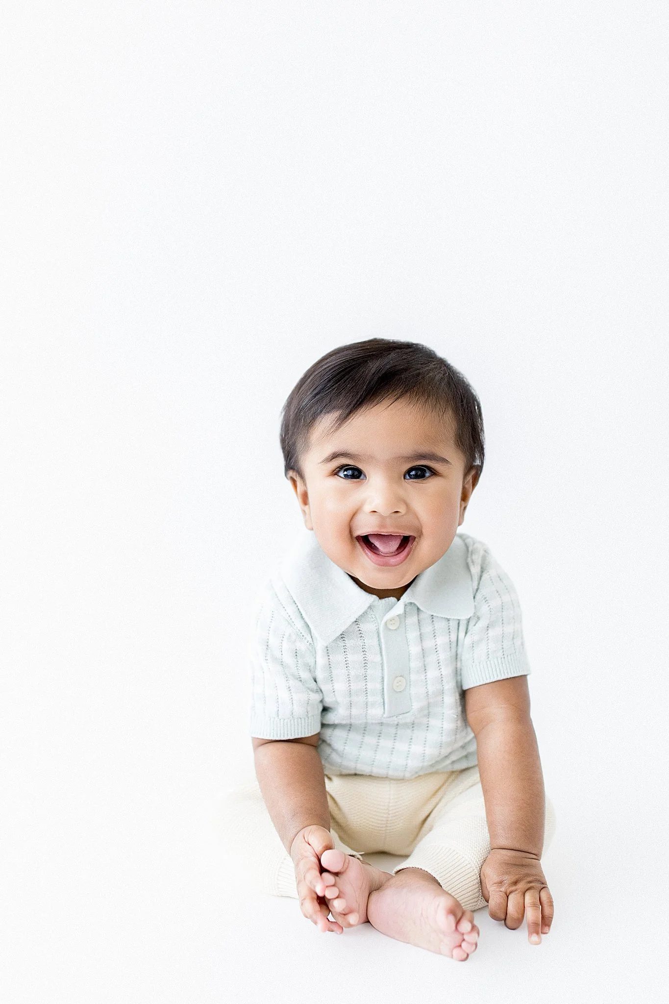 Smiling baby boy sitting on the floor against a white background for kids photography Naperville