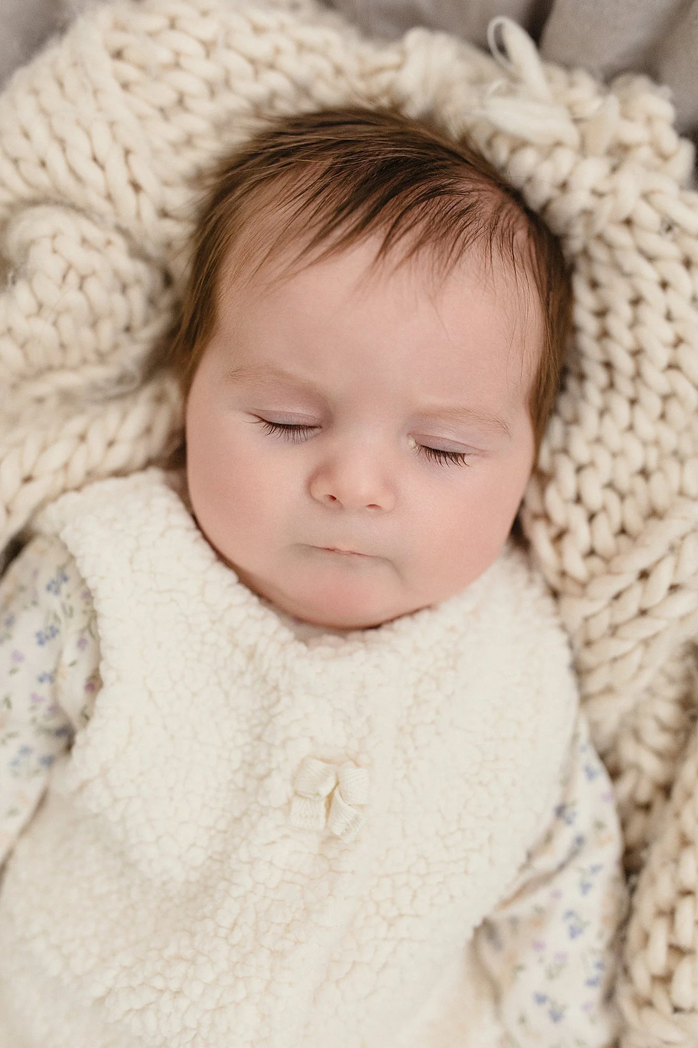 A sleeping baby with closed eyes, lying on a chunky knit blanket, wearing a cozy cream vest and patterned shirt with a newborn photographer naperville.