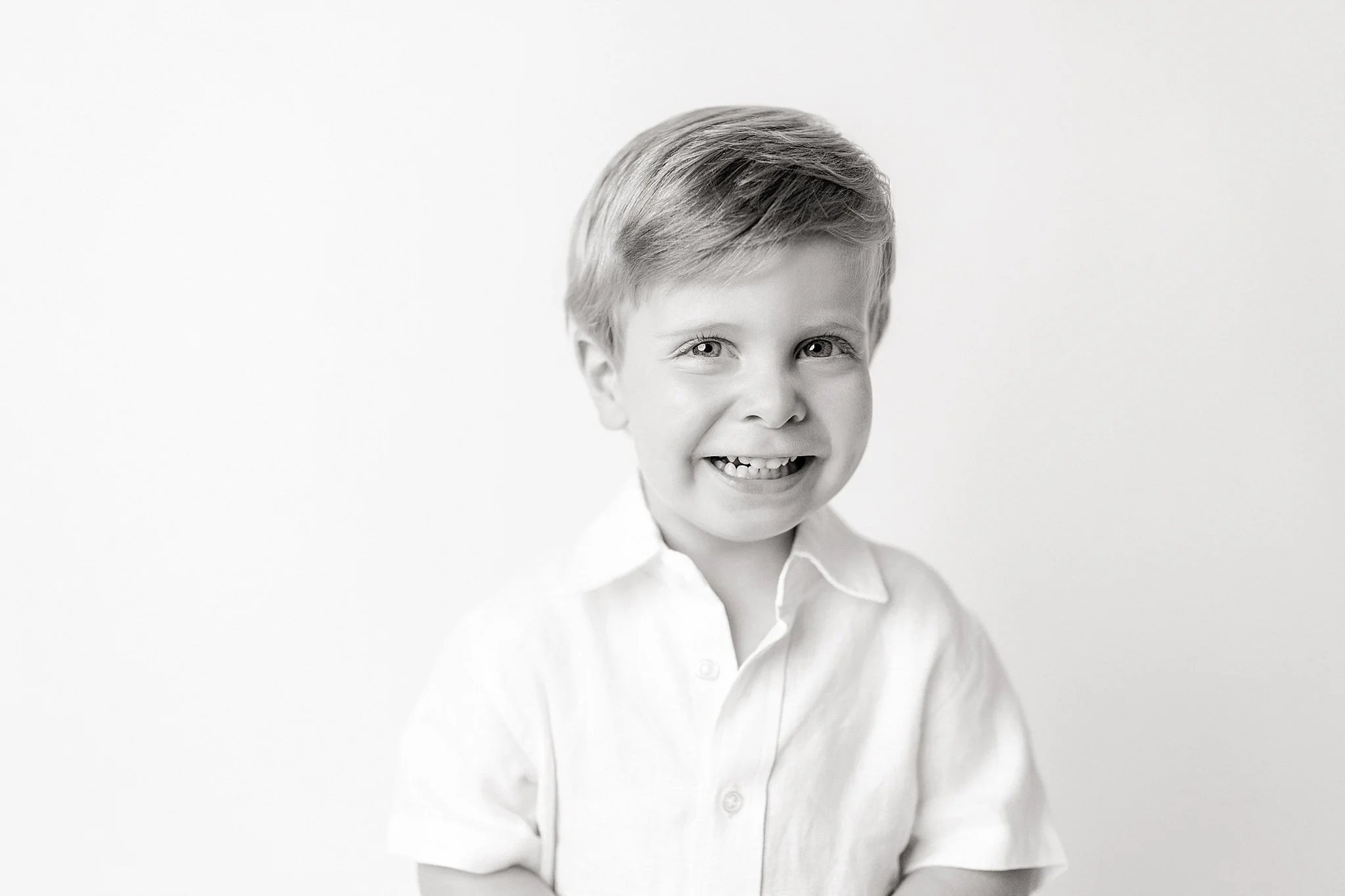 Black and white photo of a smiling young boy with short, neat hair, wearing a collared shirt, photographed against a plain light background during a personality photoshoot in Naperville, IL.
