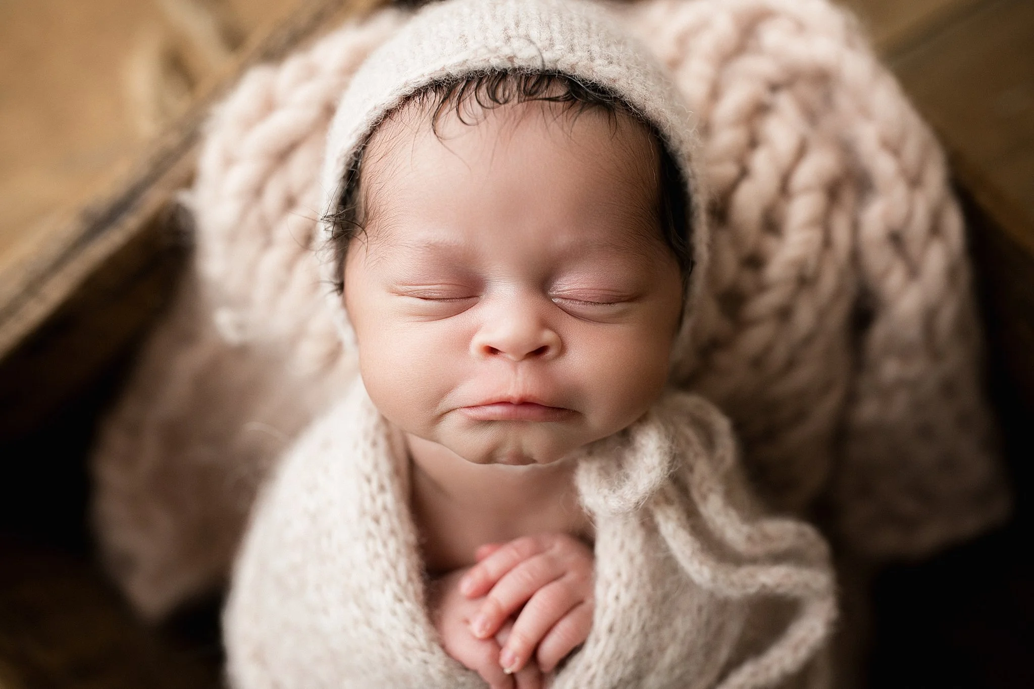 Close-up of a sleeping baby wearing a cozy knit hat and wrapped in a matching knit blanket, lying on a soft surface during a newborn session with Naperville newborn photographer Marie Lopez.