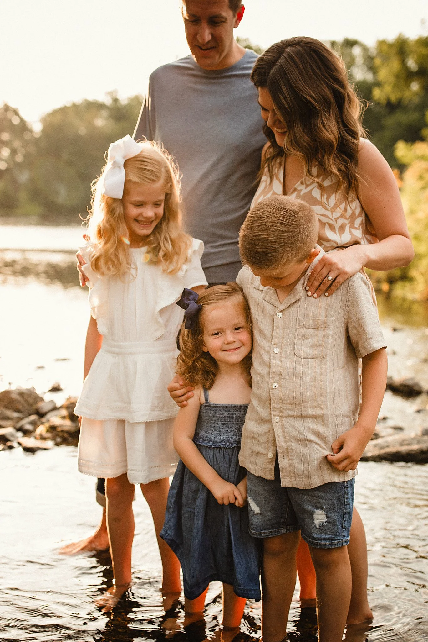 A family of five standing in a water during sunset, smiling during a family creek mini session with Ally and B Photography in Oswego, IL.