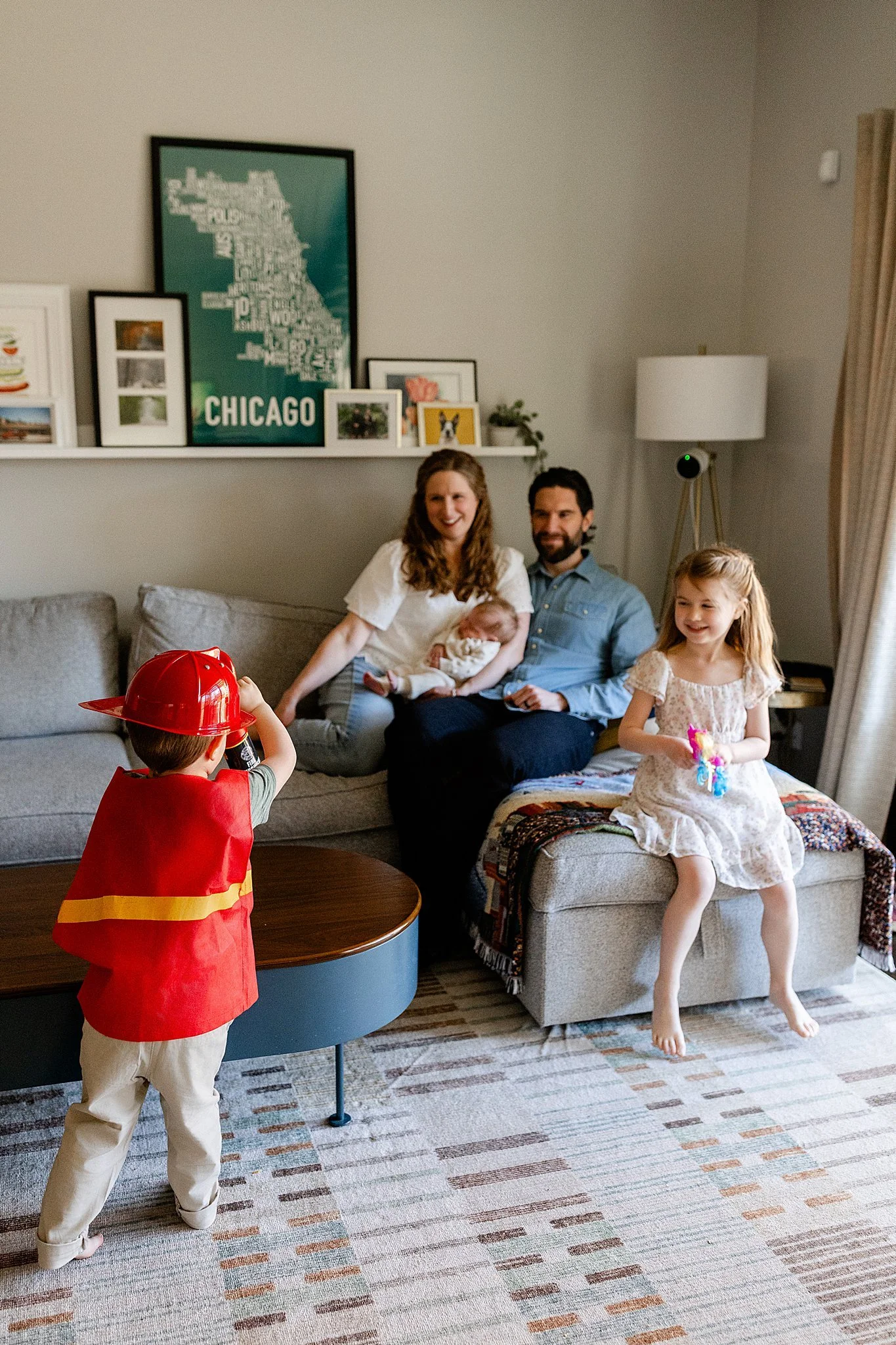 A family of four with a baby, a young girl, and two adults sitting on a couch in a living room celebrating a birthday for lifestyle photos in Elmhurst, IL.