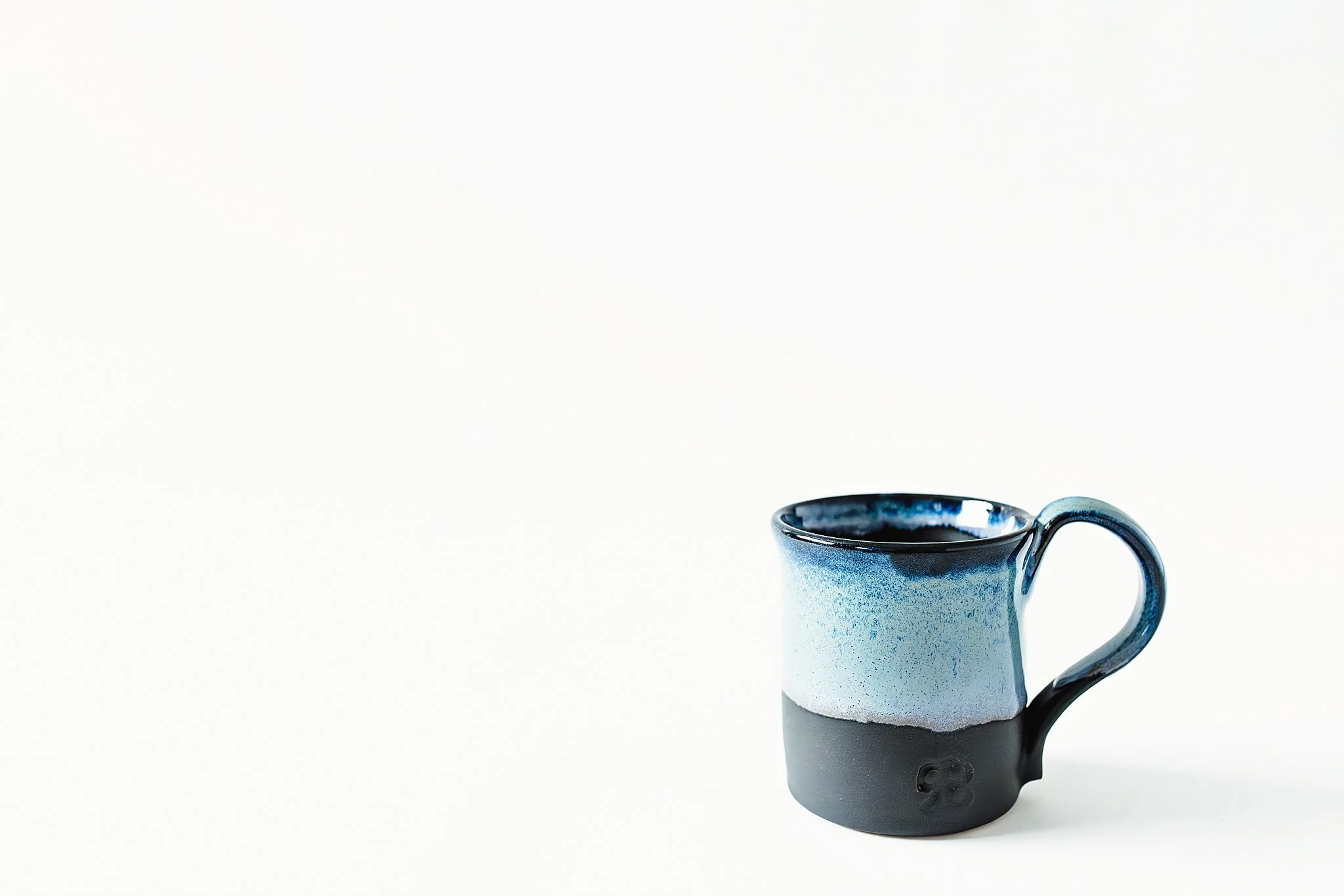 Blue and black ceramic mug with a small flower design on the lower part of the mug, set against a plain white background for product photography.