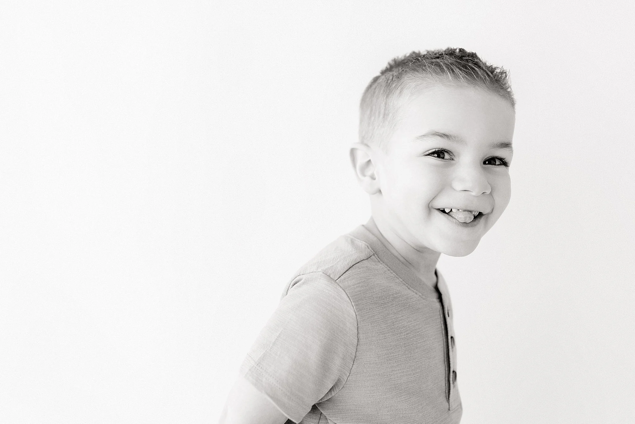 Black and white photo of a smiling young boy with short hair, wearing a short-sleeved shirt, standing against a plain background for photo studios in downtown Naperville.