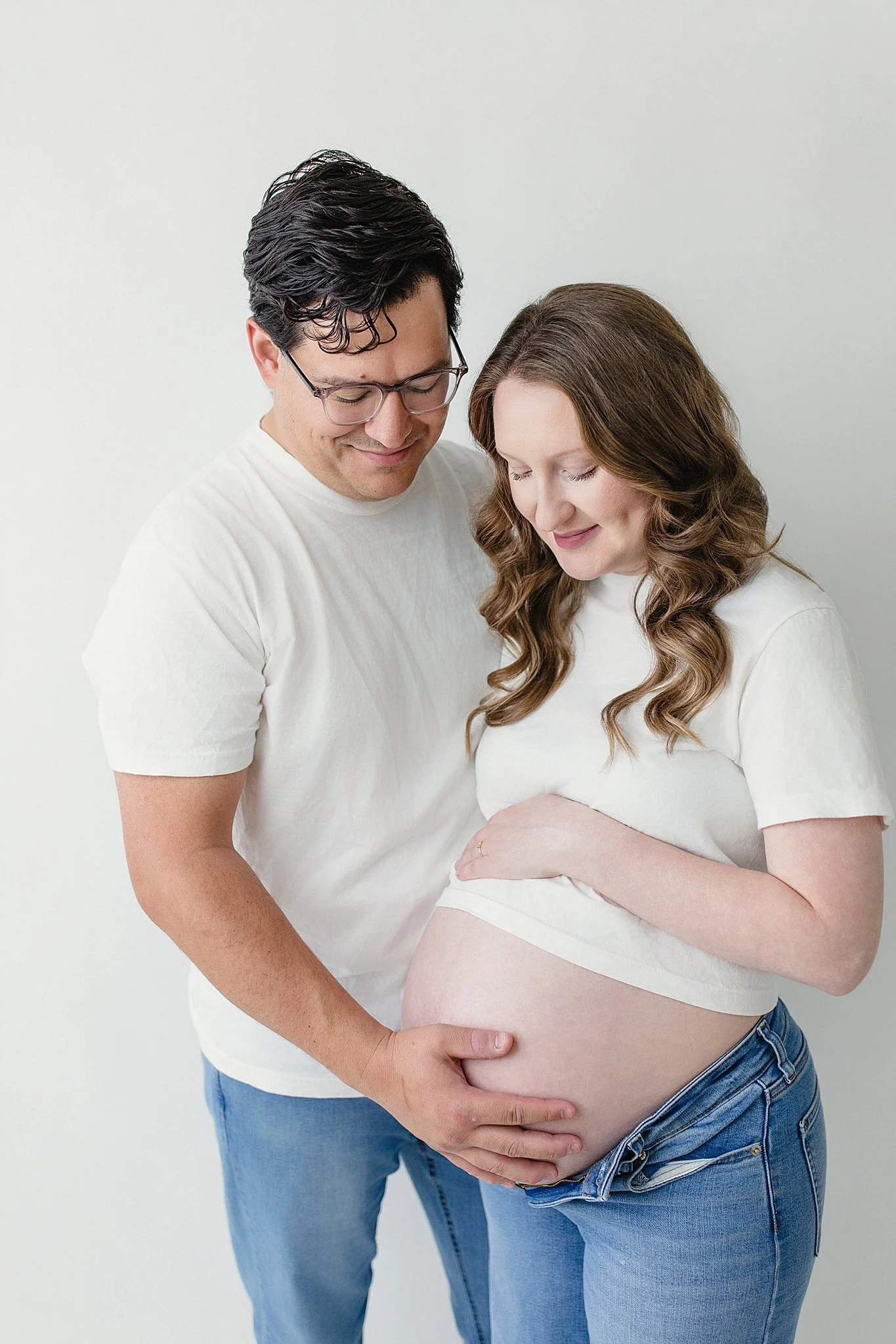 A man and pregnant woman are standing close together, with the man gently holding the woman's belly and both smiling with their eyes closed with the best Naperville maternity photographer.