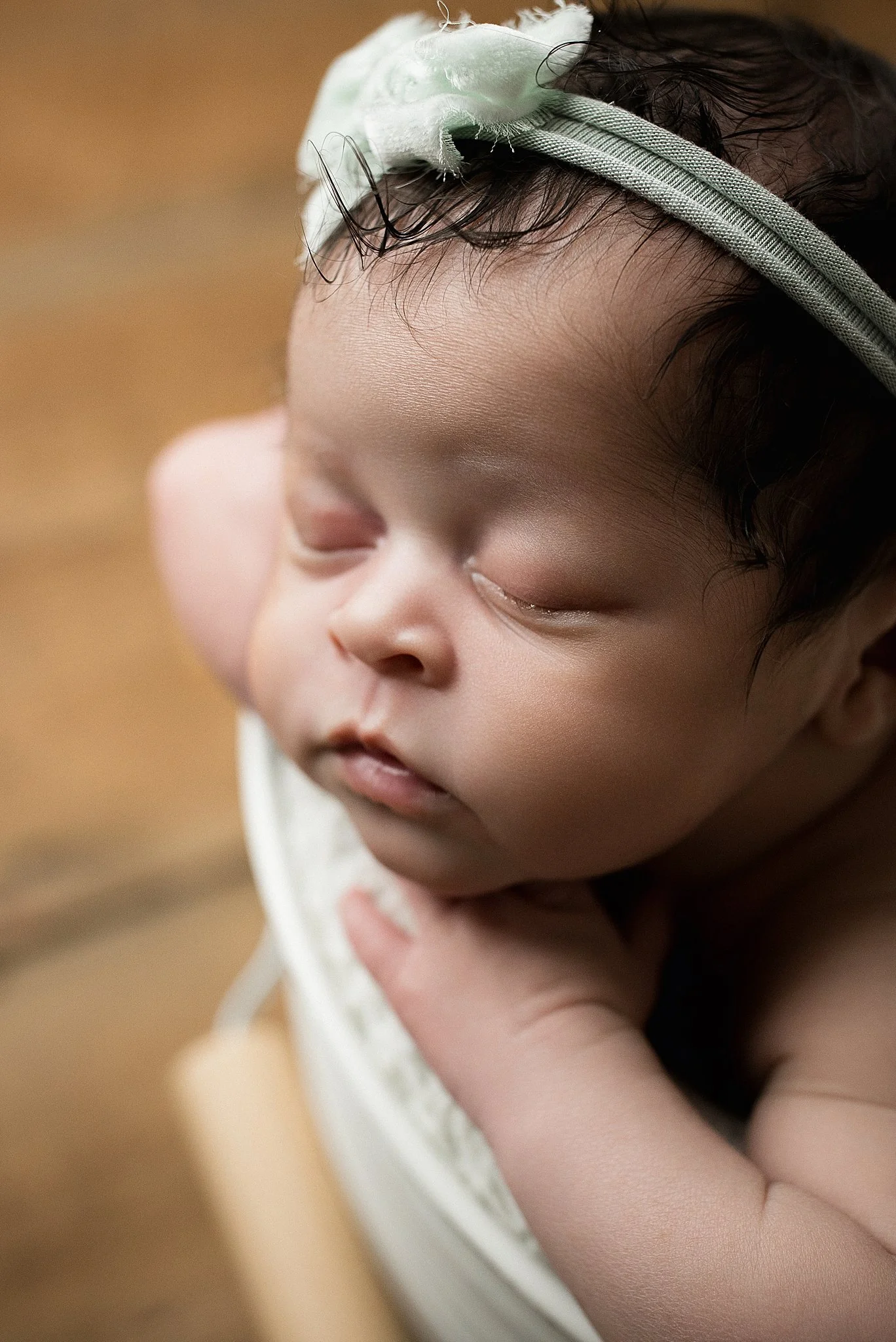 A close-up of a baby sleeping peacefully, wearing a white headband with a bow, and resting its chin on its folded arm during a newborn session with Naperville newborn photographer.