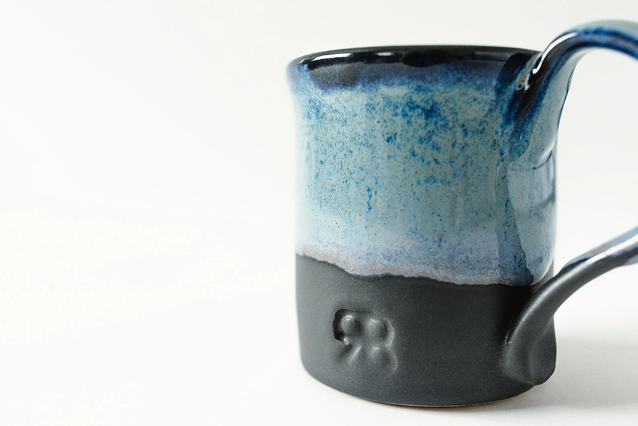 A ceramic mug with a black base and a glossy blue and cream glaze on the upper part, with a handle on the right side for product photography Naperville.