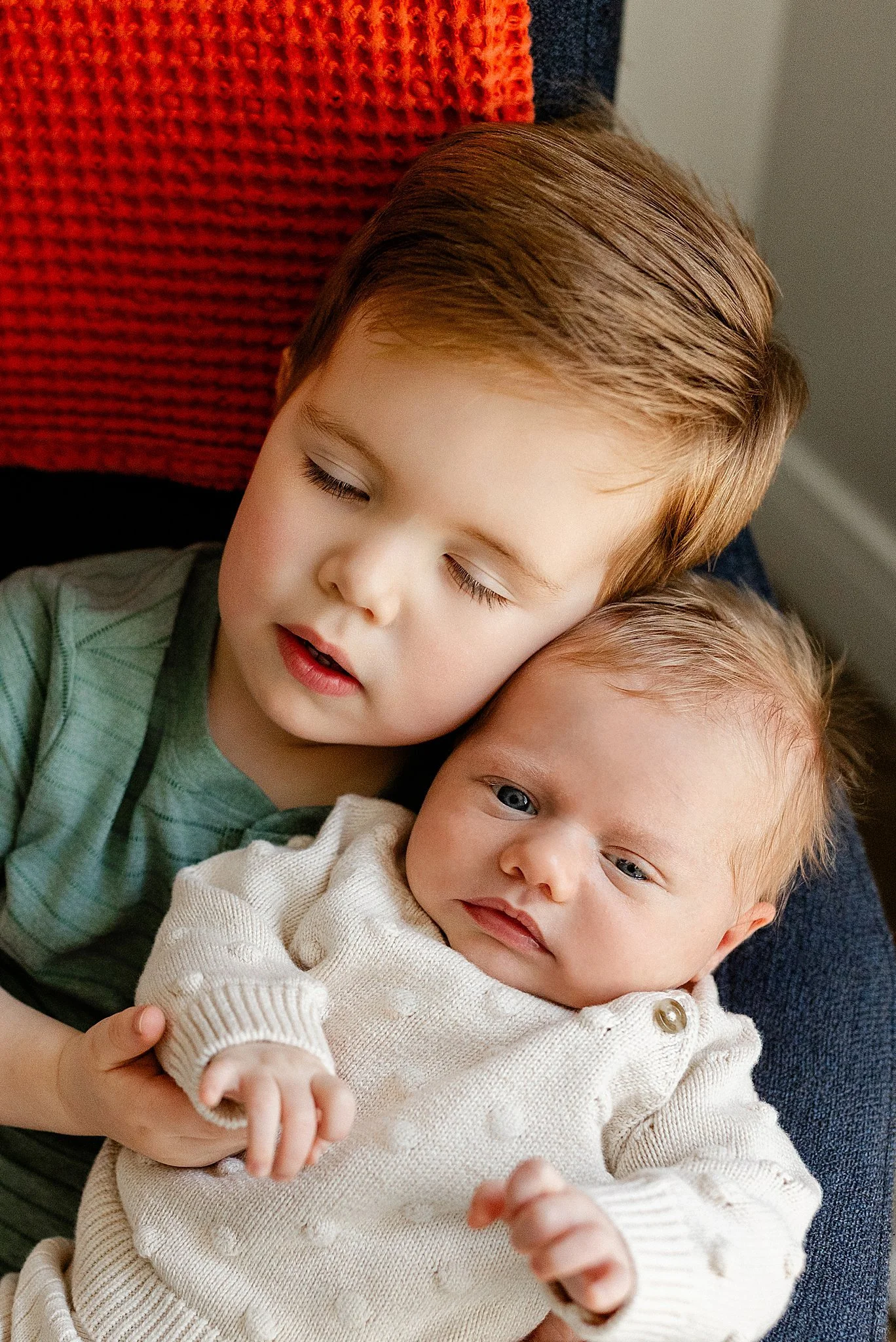 Two young children, a boy with light brown hair and a girl with blonde hair, are sleeping close together, with the girl resting her head on the boy's shoulder.