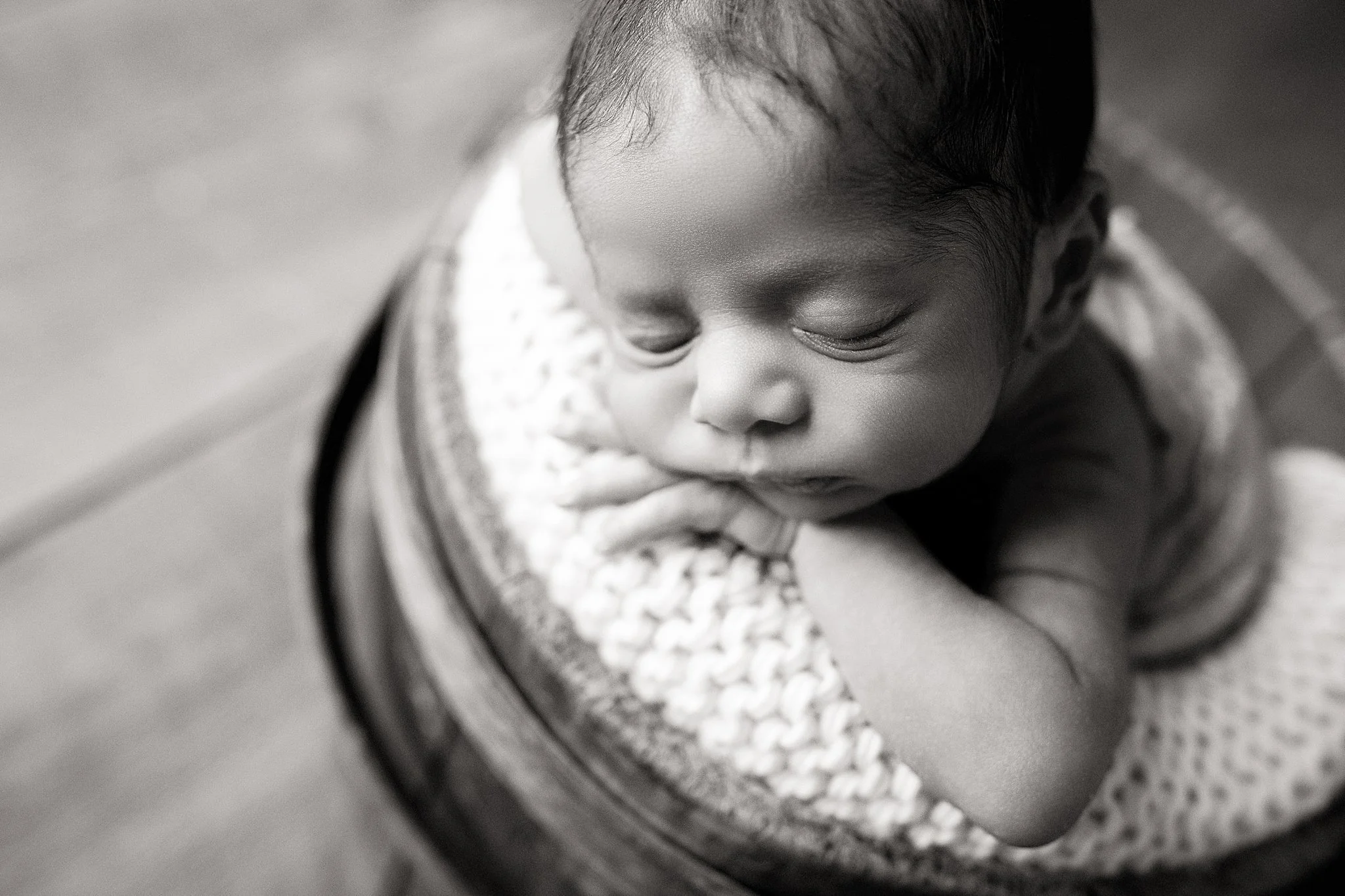 Black and white photo of a sleeping baby cuddling a knitted blanket for a newborn session with Marie Lopez in Naperville.