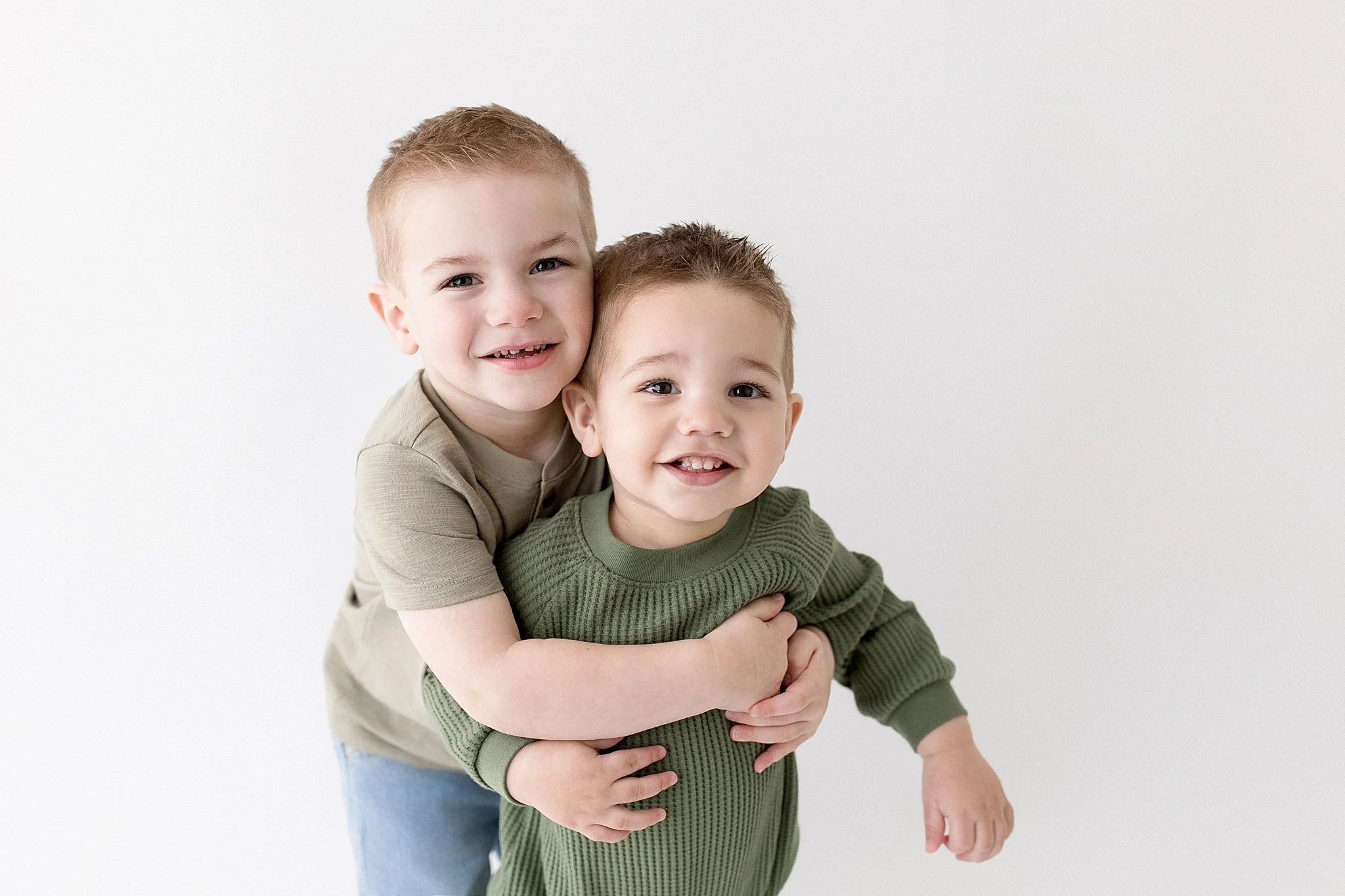 Two young boys hugging and smiling at the camera against a plain white background with naperville photographer Marie Lopez.