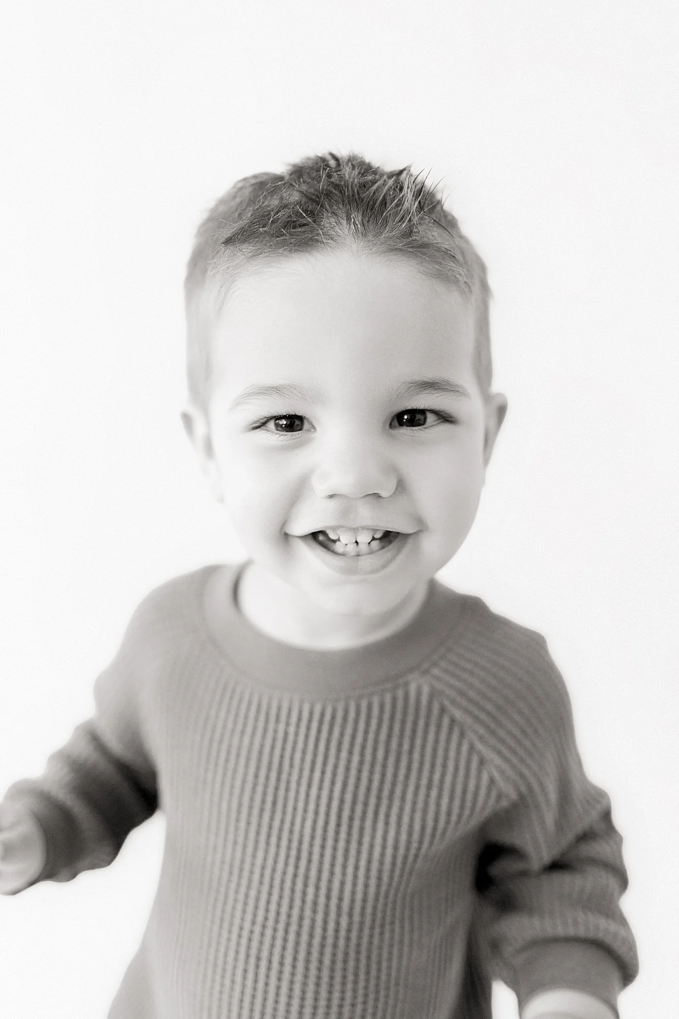 Black and white photo of a smiling young boy with short hair, wearing a ribbed shirt with a baby photographer in Naperville, IL.