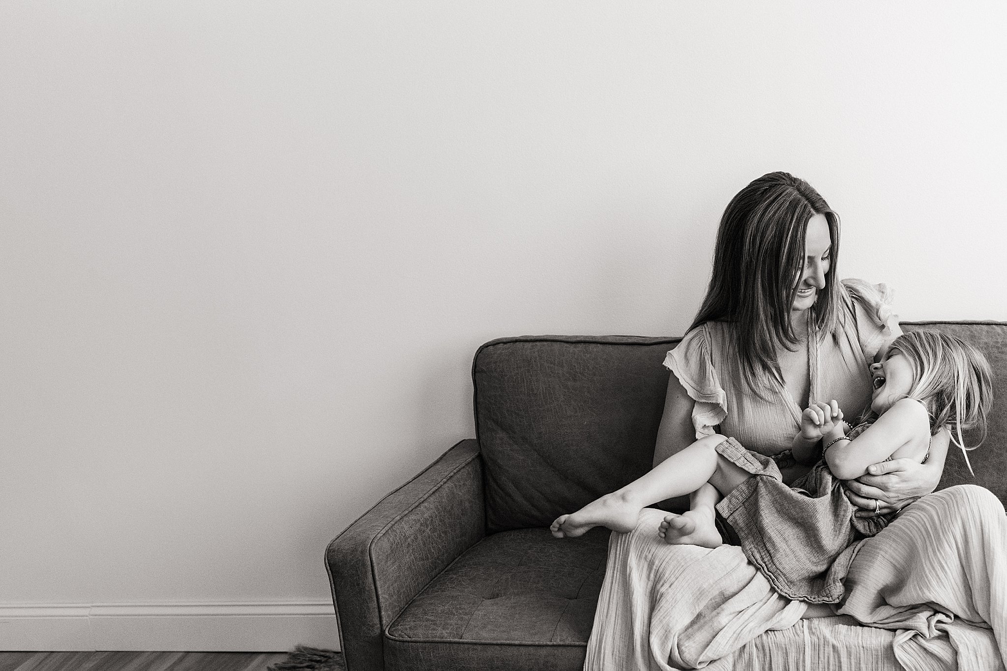 A woman and a young girl sitting on a couch, laughing and playing together.