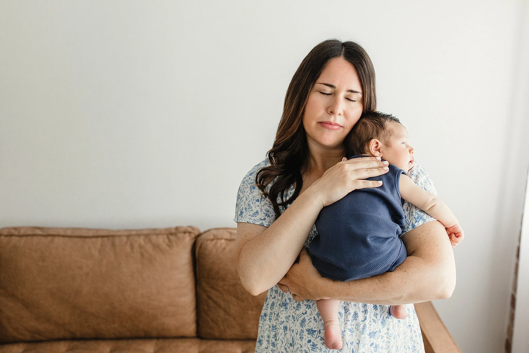 A woman holding a young child in her arms, gently resting her forehead on the child's head with her eyes closed during a lifestyle newborn photoshoot in Naperville.
