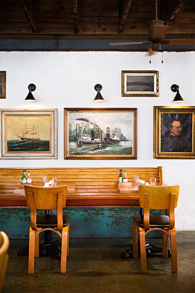 A straight row of art accentuated by overhead lighting, at Leon's Fine Poultry and Oysters in Charleston, South Carolina. Photo by Brittany Ambridge for Domino . 