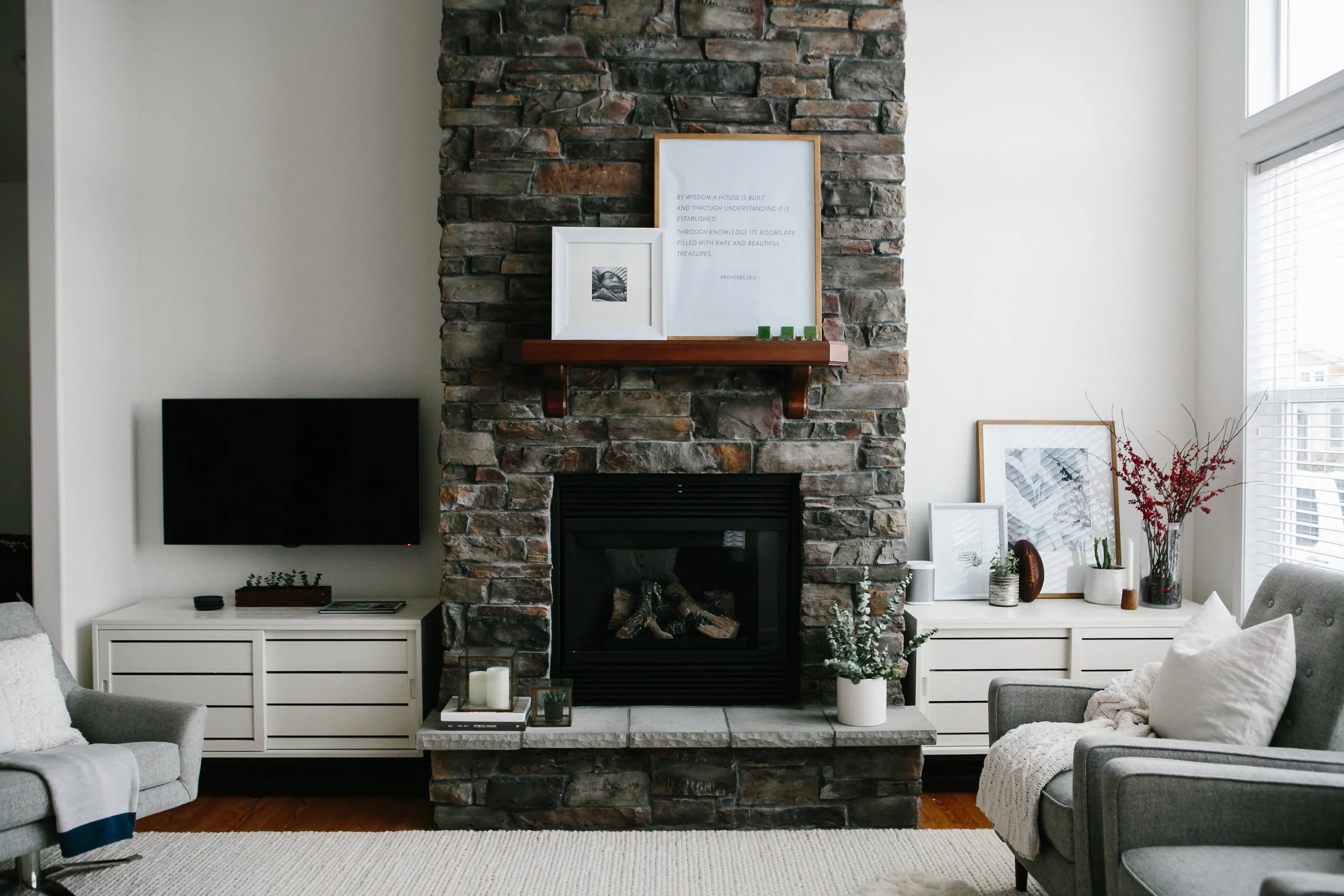 Natural stone grand fireplace with white Crate and Barrel base cabinets in a modern coastal home.