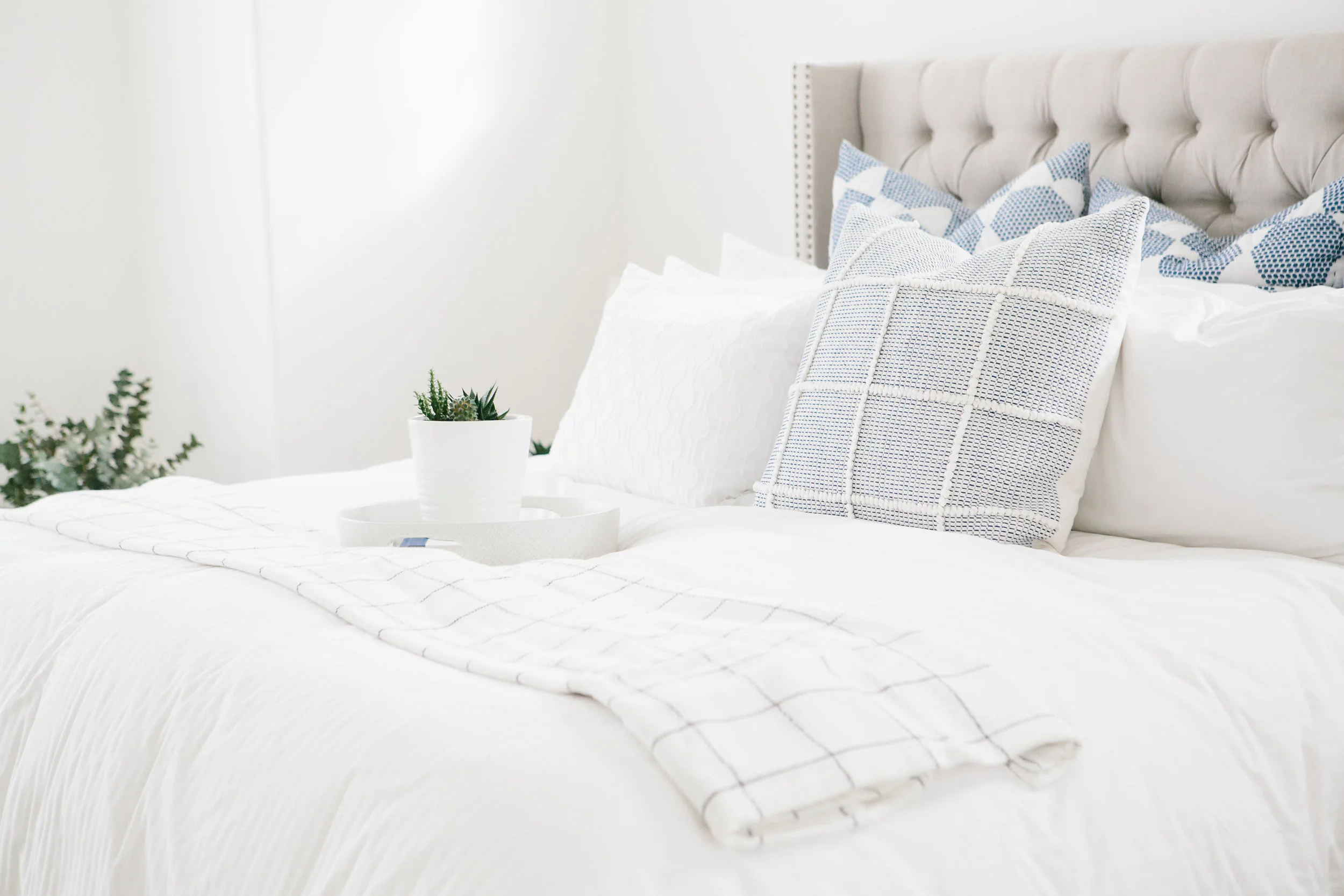 A white guest bed with navy blue accent pillows, a throw planket and a round tray.
