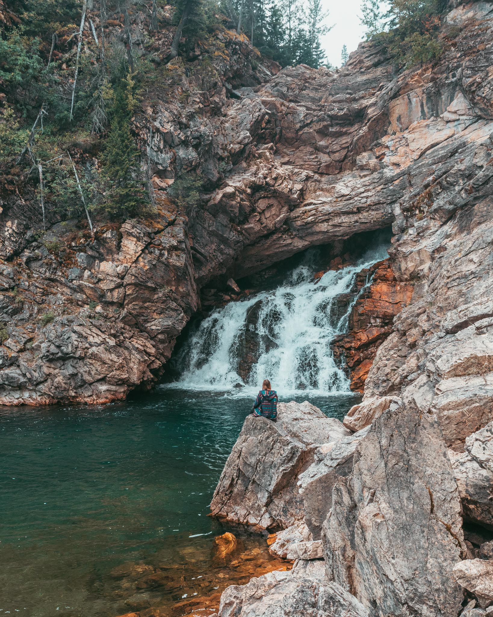 Girl sitting at Running Eagle Falls in Glacier National Park Montana