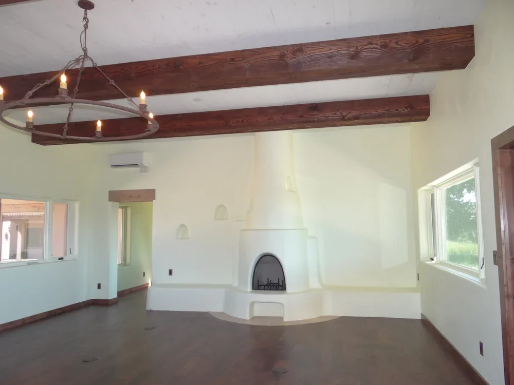 A spacious empty room featuring a fireplace and exposed wooden beams on the ceiling.